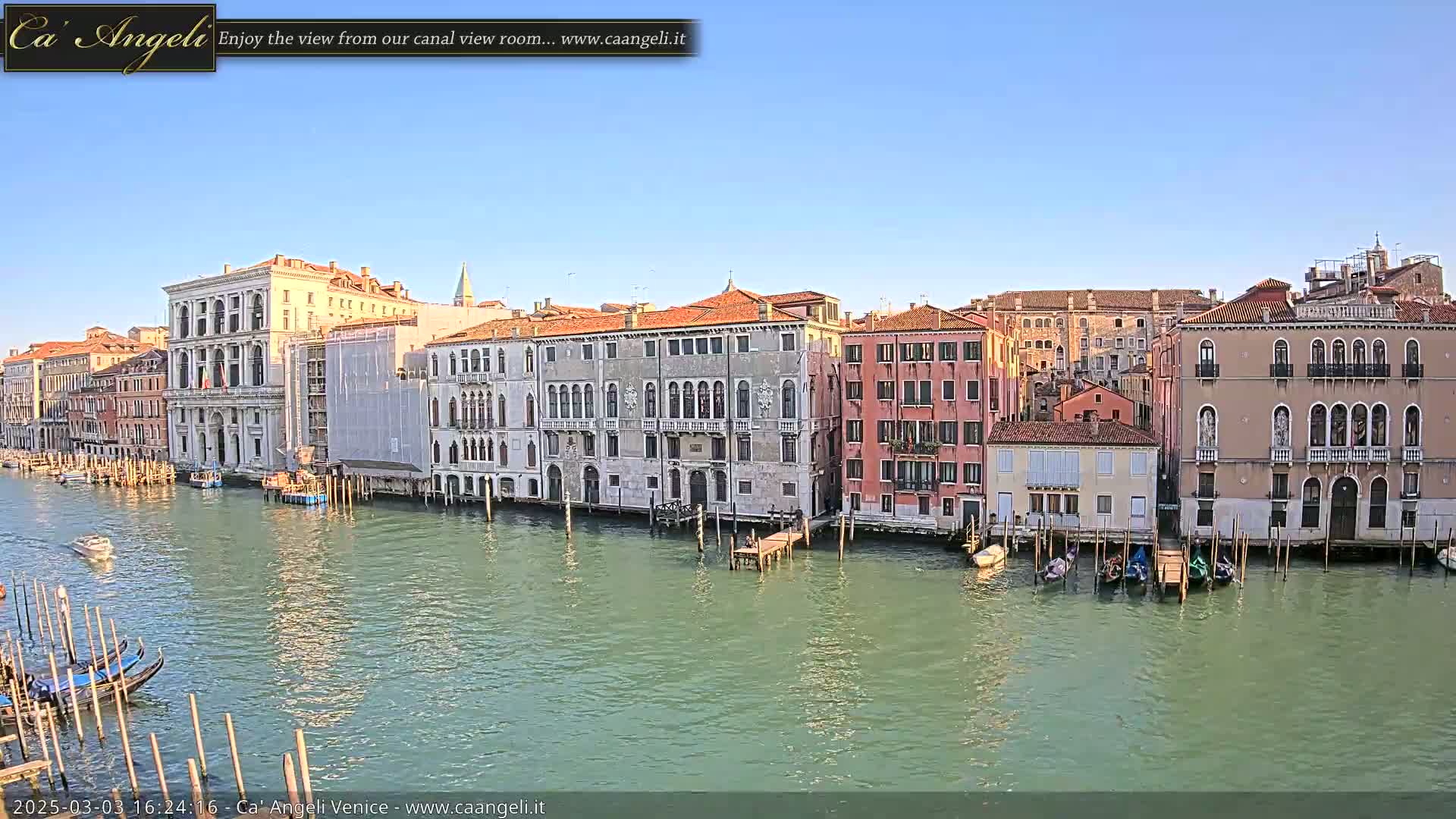 A sunny day in Venice shows a canal lined with historic buildings and several gondolas moored along the waterfront.
