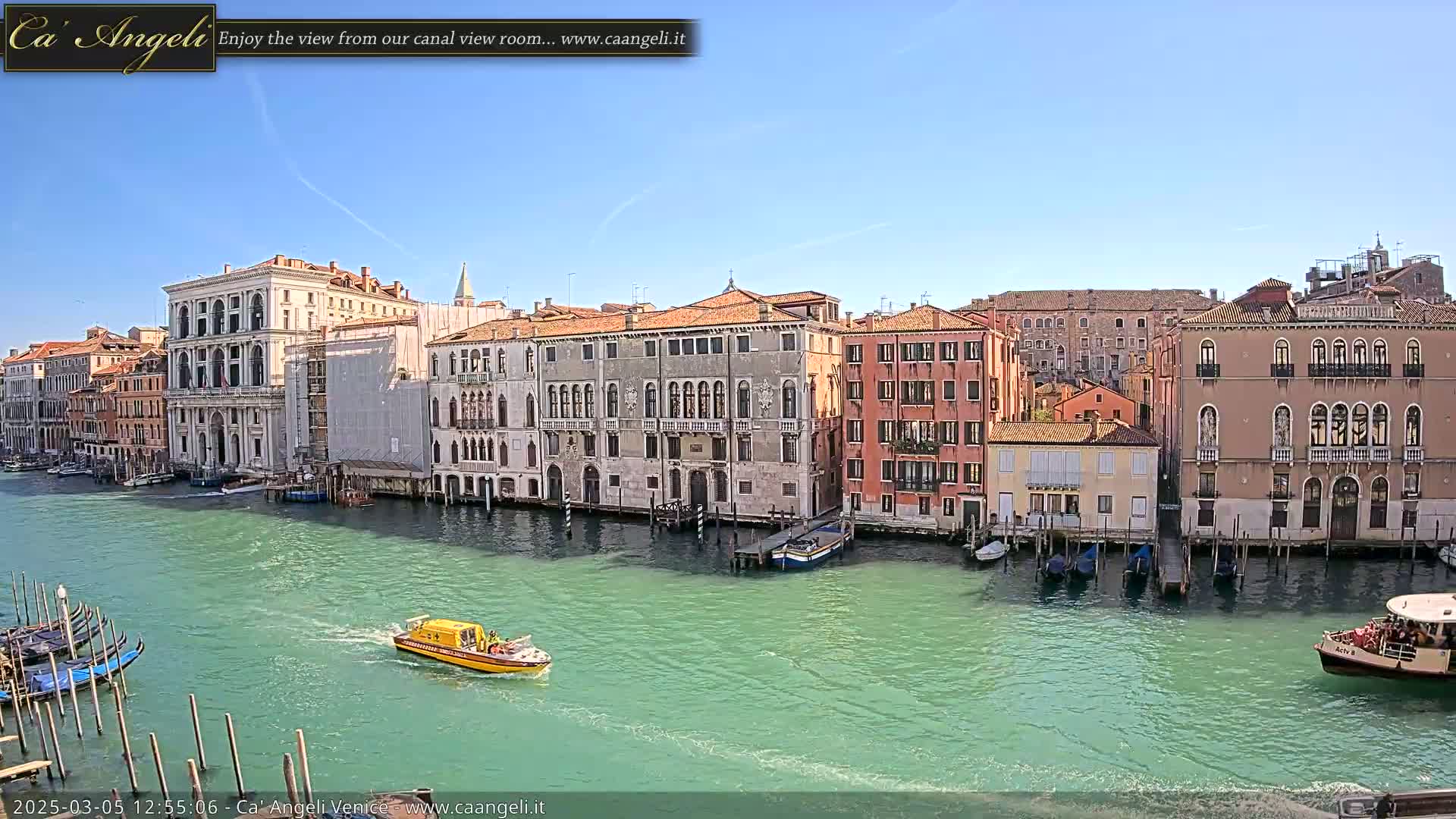 A sunny day in Venice shows a canal lined with tall buildings, with several boats, including a water taxi and gondolas, on the water.