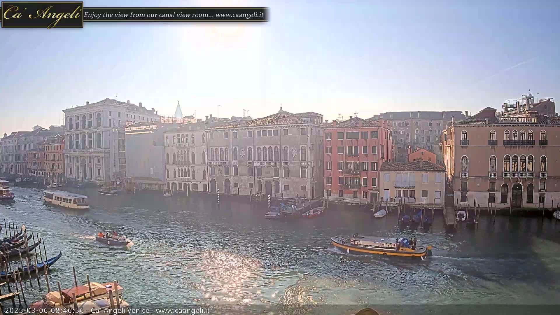 A sunny day in Venice shows several boats on a canal lined with historic buildings.