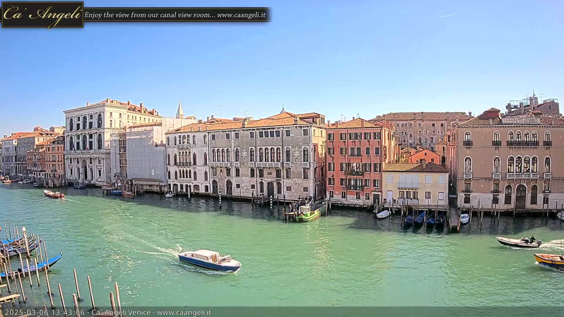 A sunny day in Venice shows several historic buildings lining a canal, with gondolas and motorboats on the water.