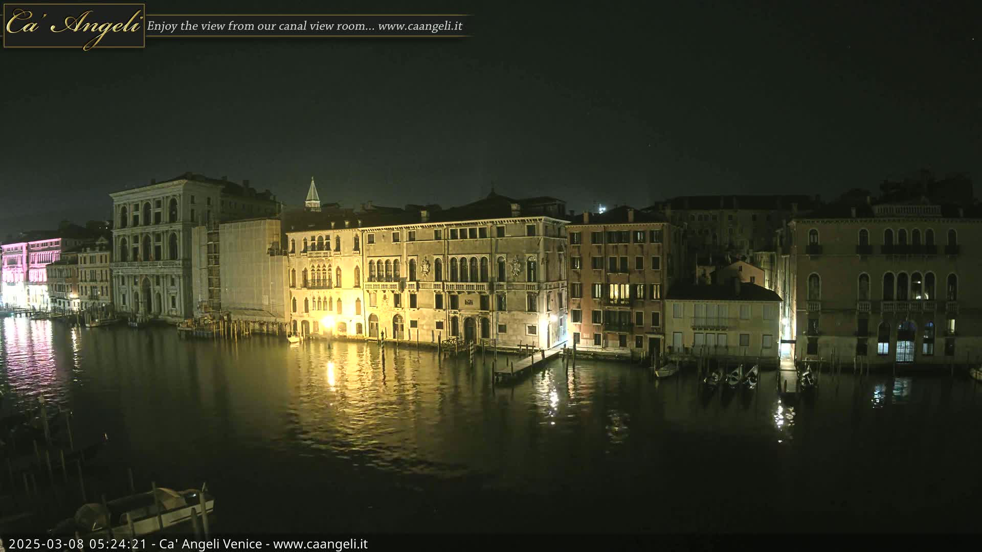 A nighttime view of a canal in Venice, Italy, with several illuminated buildings lining the waterway.