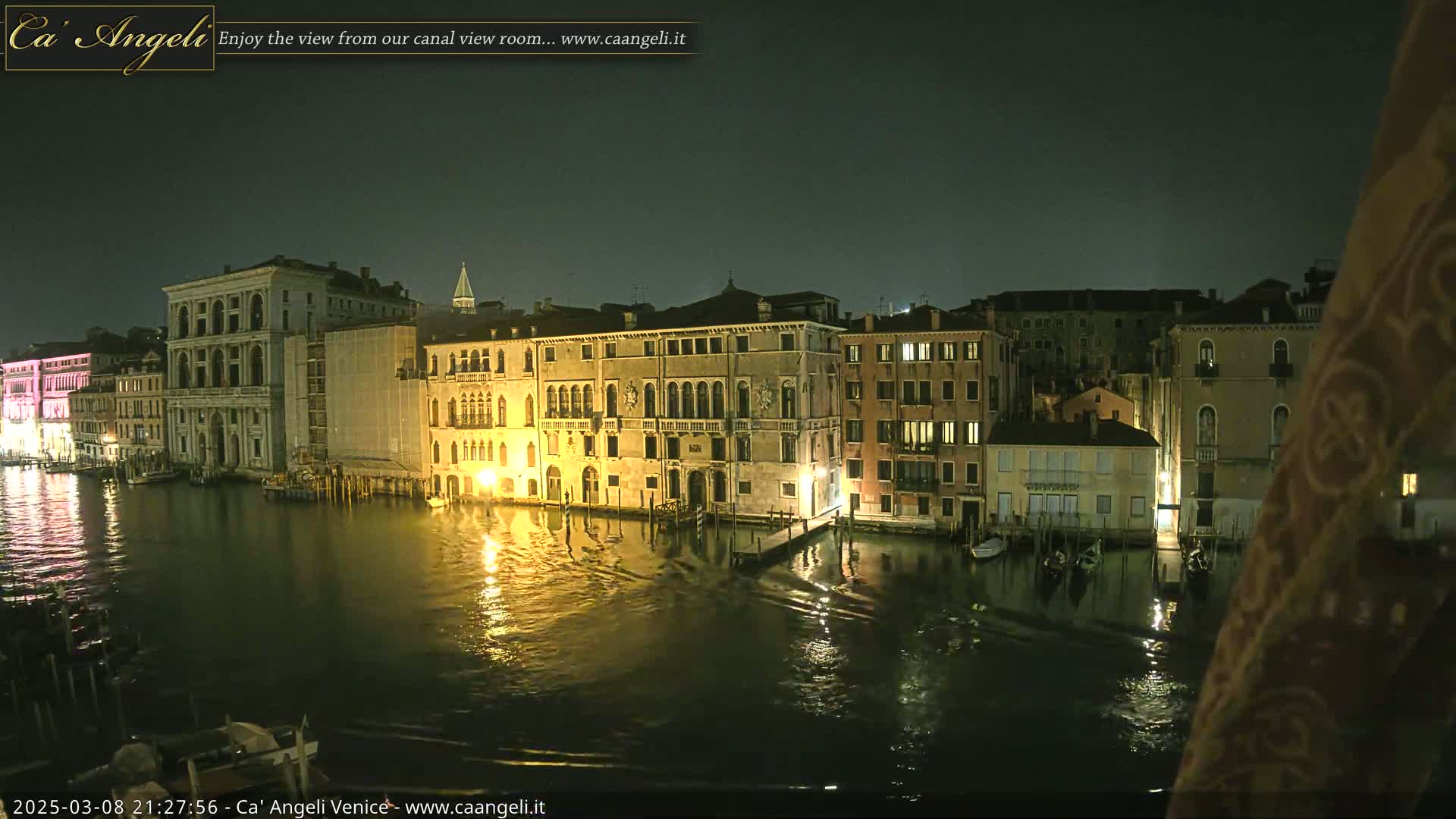 Nighttime view of a canal in Venice, Italy, with illuminated buildings lining the waterway under a dark sky.