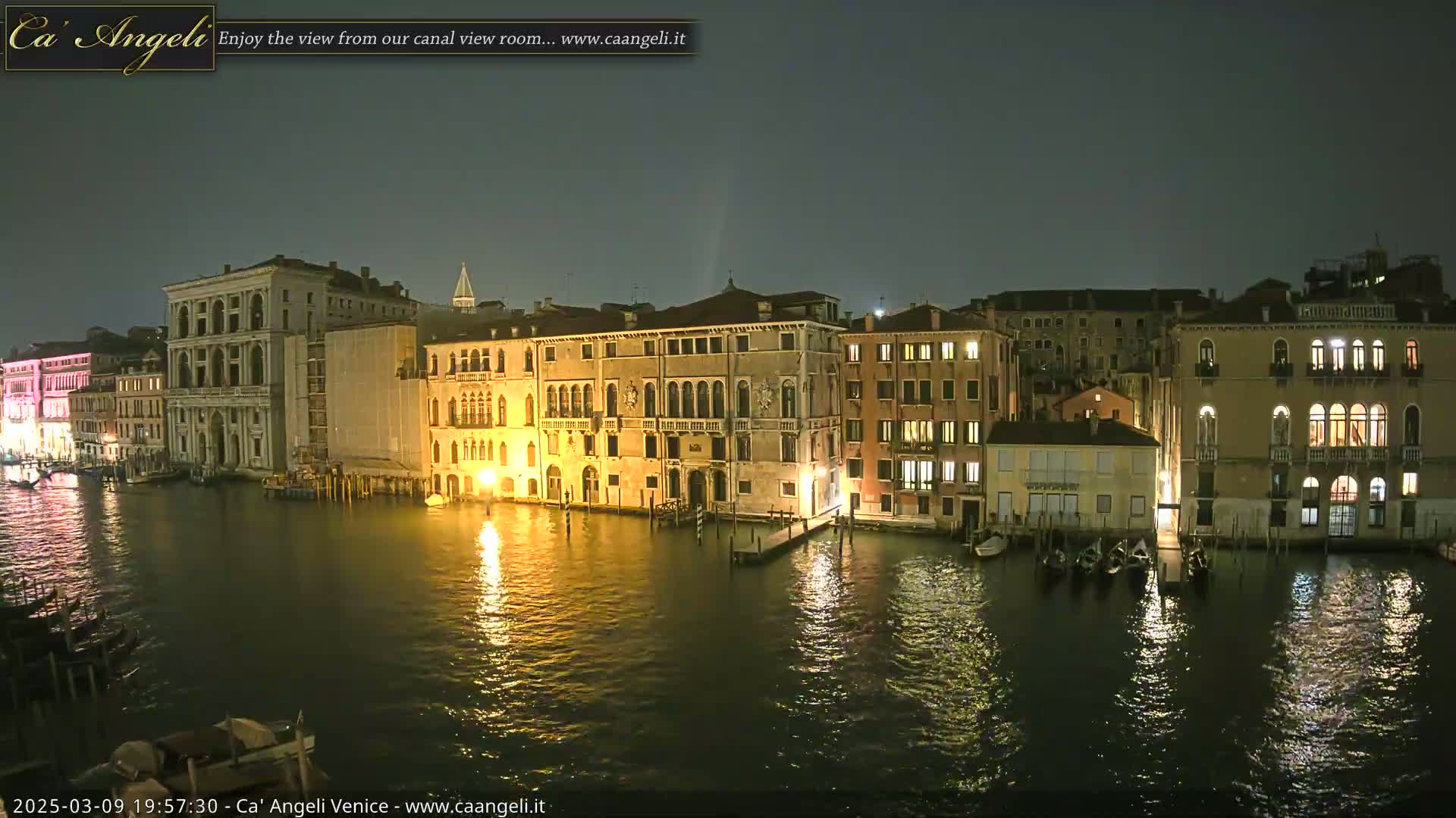 A nighttime view of illuminated buildings lining a calm canal in Venice.