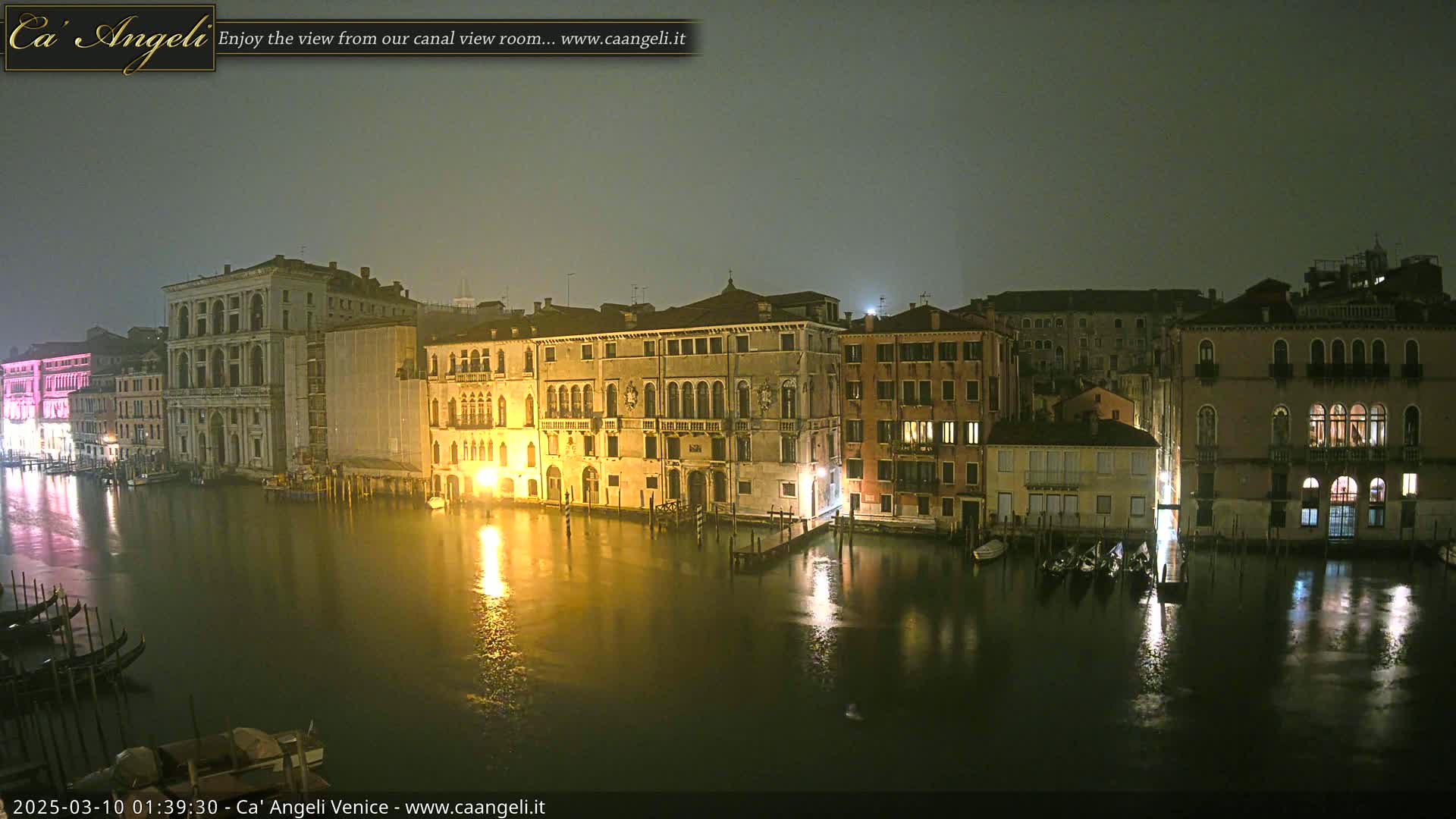Nighttime view of illuminated buildings lining a canal in Venice, under a foggy sky.