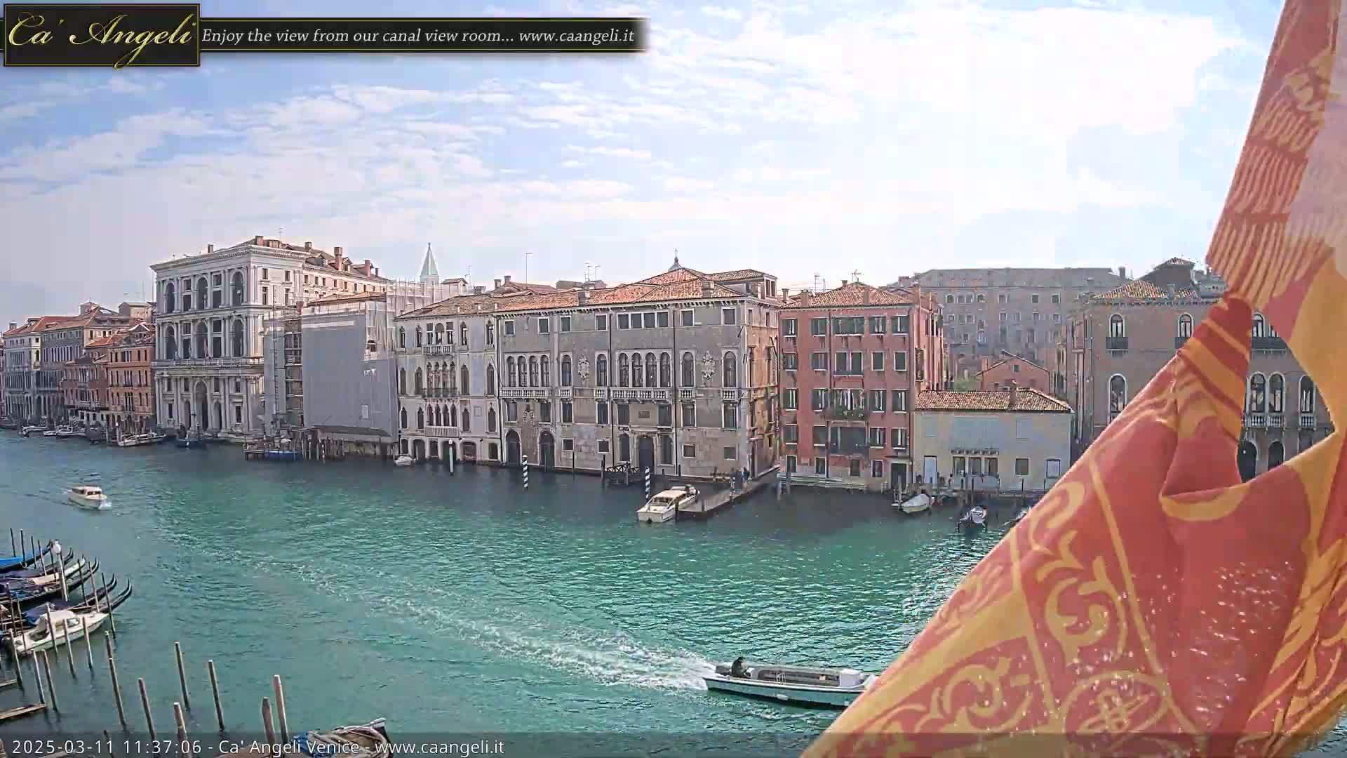 A Venetian canal with several boats and buildings lining the waterway under a partly cloudy sky.