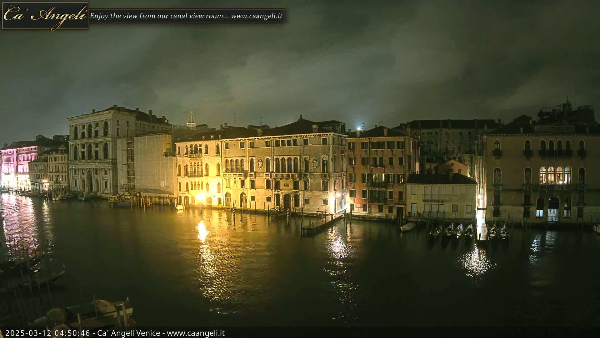 Nighttime view of illuminated buildings along a canal, under a cloudy sky.