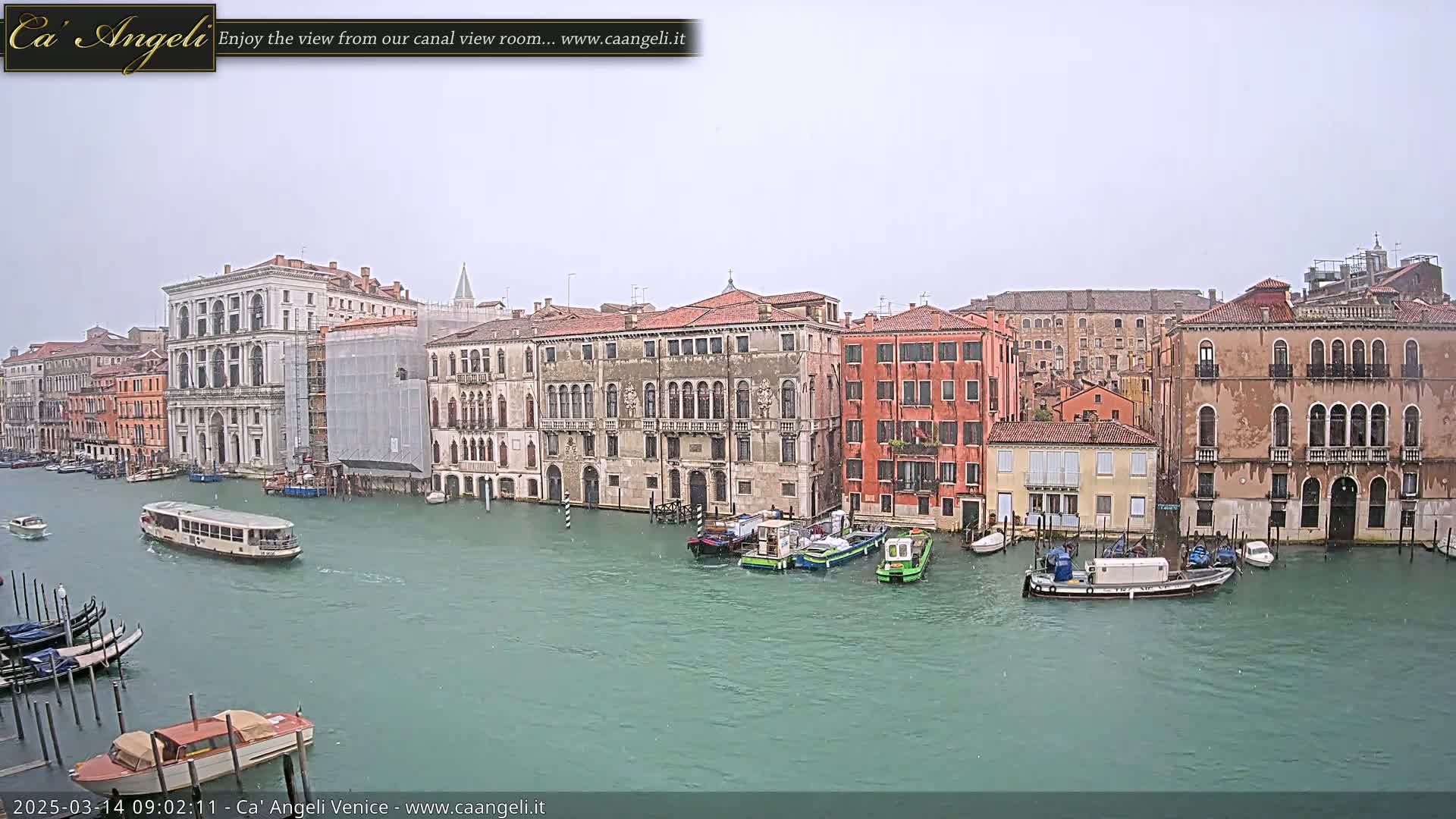 A waterway in Venice, Italy, shows several buildings along its edge on an overcast day with light rain.