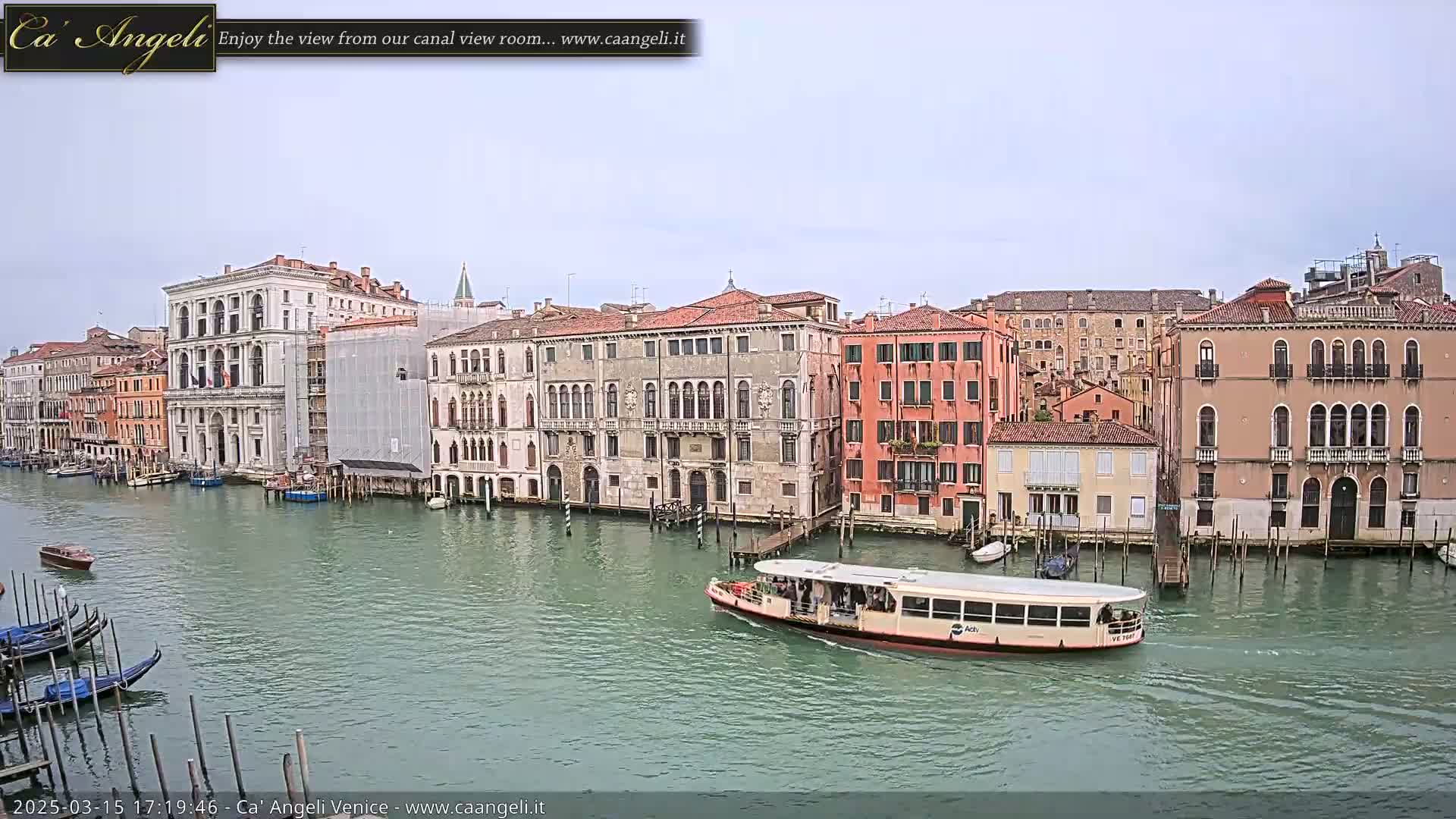 A waterway in Venice, Italy, shows several historic buildings lining the canal under an overcast sky, with a passenger boat passing by.