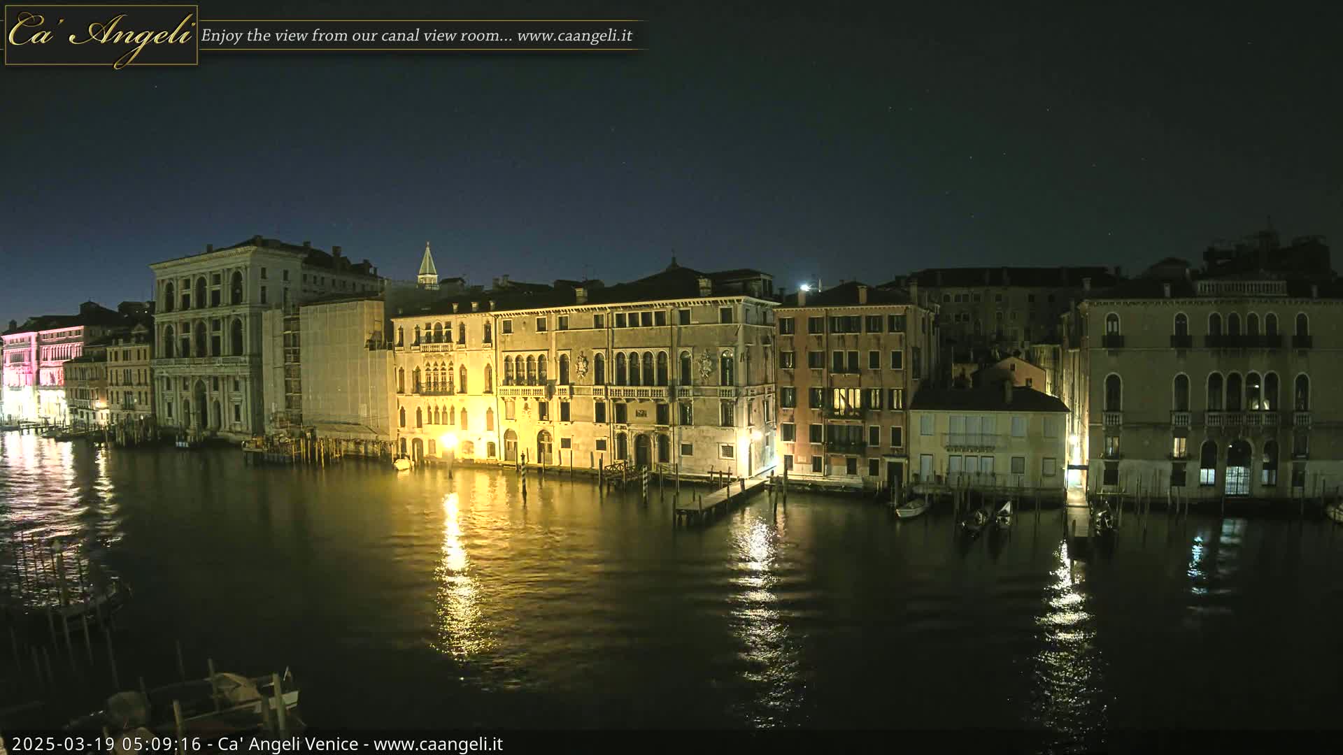 A nighttime view of illuminated buildings lining a calm canal under a clear, dark sky.