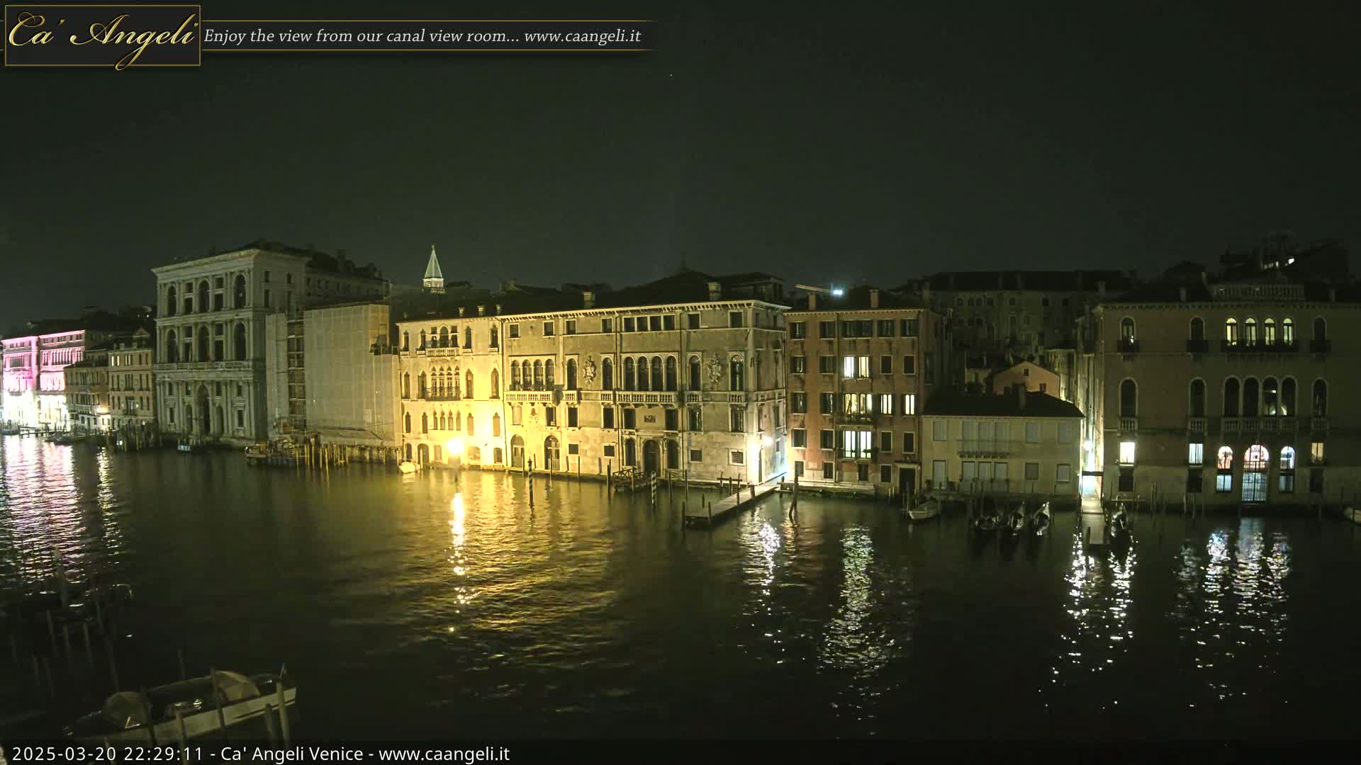 A nighttime view of a canal in Venice, showing illuminated buildings reflected in calm water.