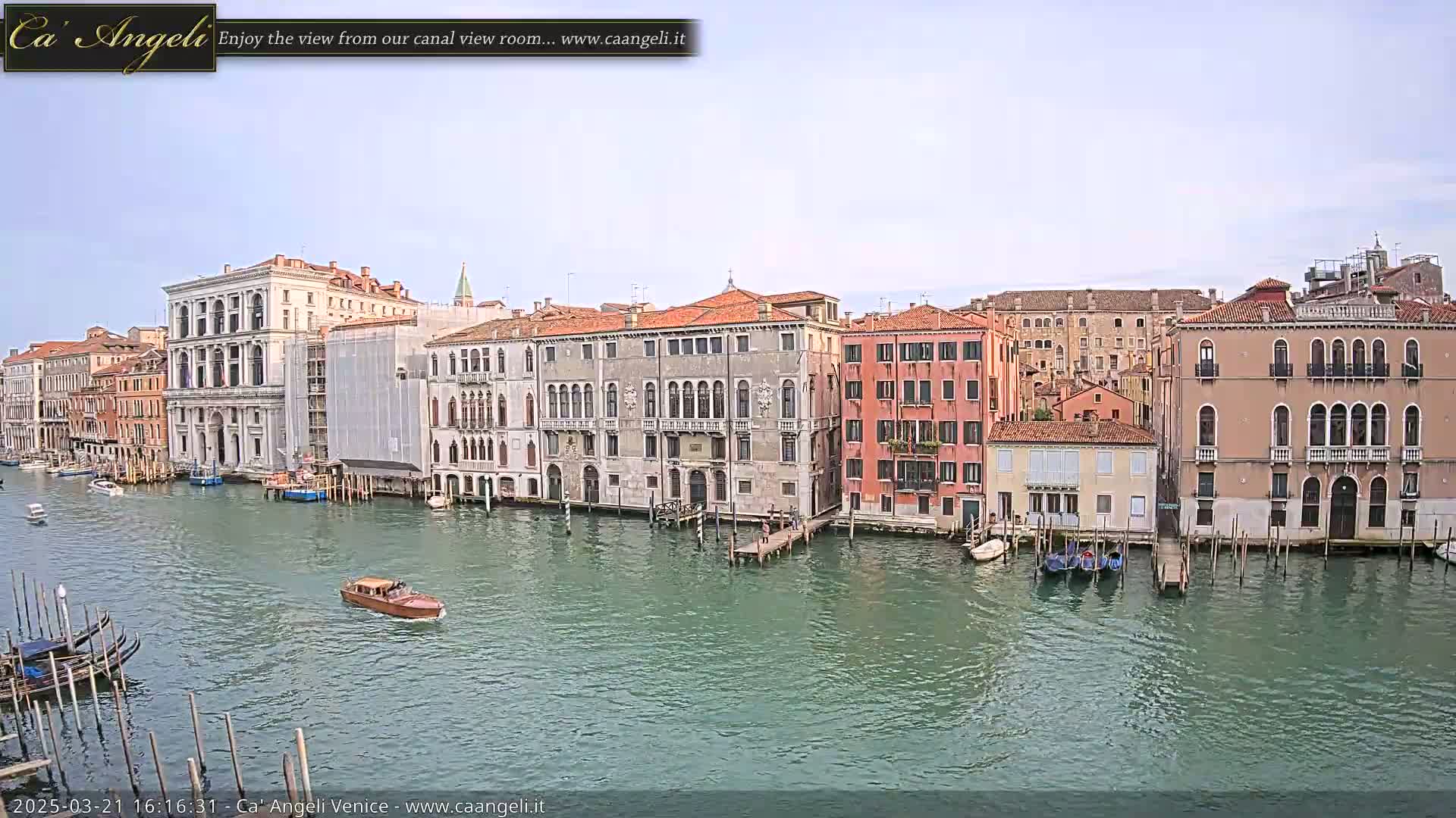 A canal in Venice, under a mostly clear sky, is lined with historic buildings, and several boats are on the water.