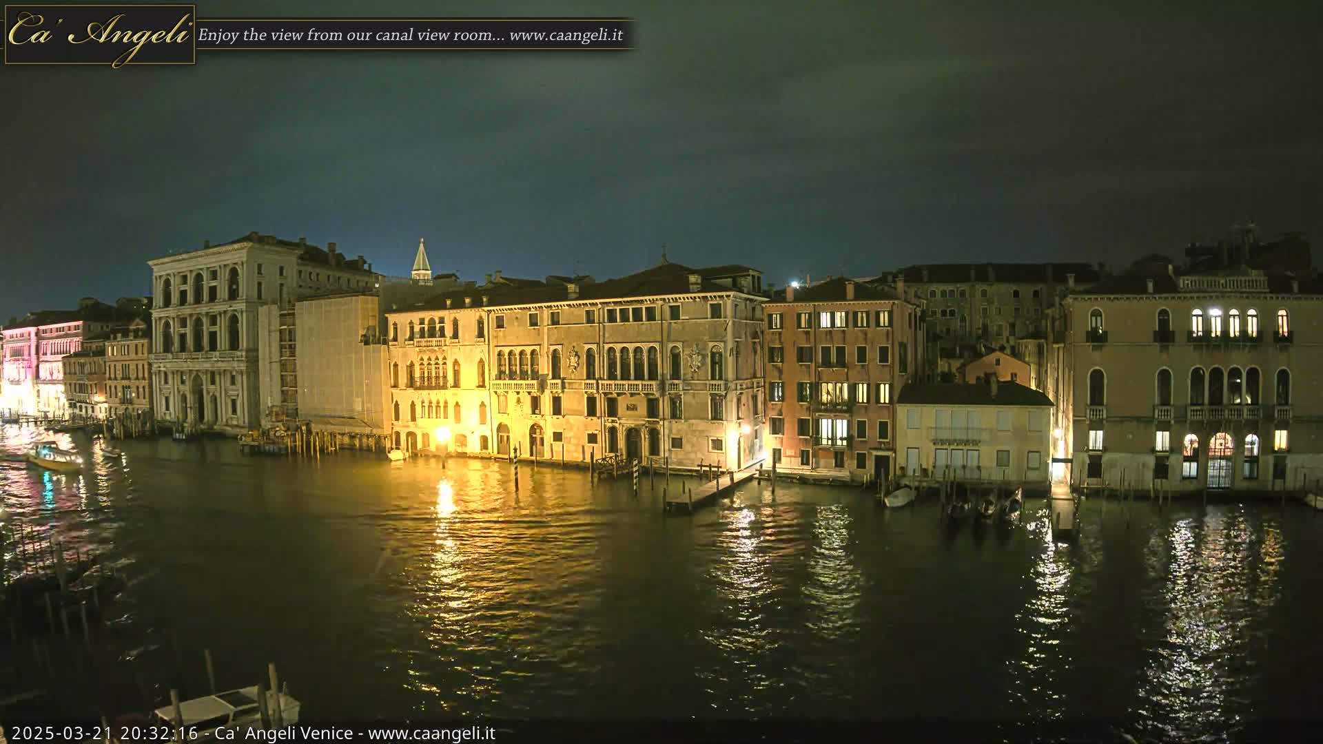 A nighttime view of illuminated buildings lining a canal, under a dark, cloudy sky.