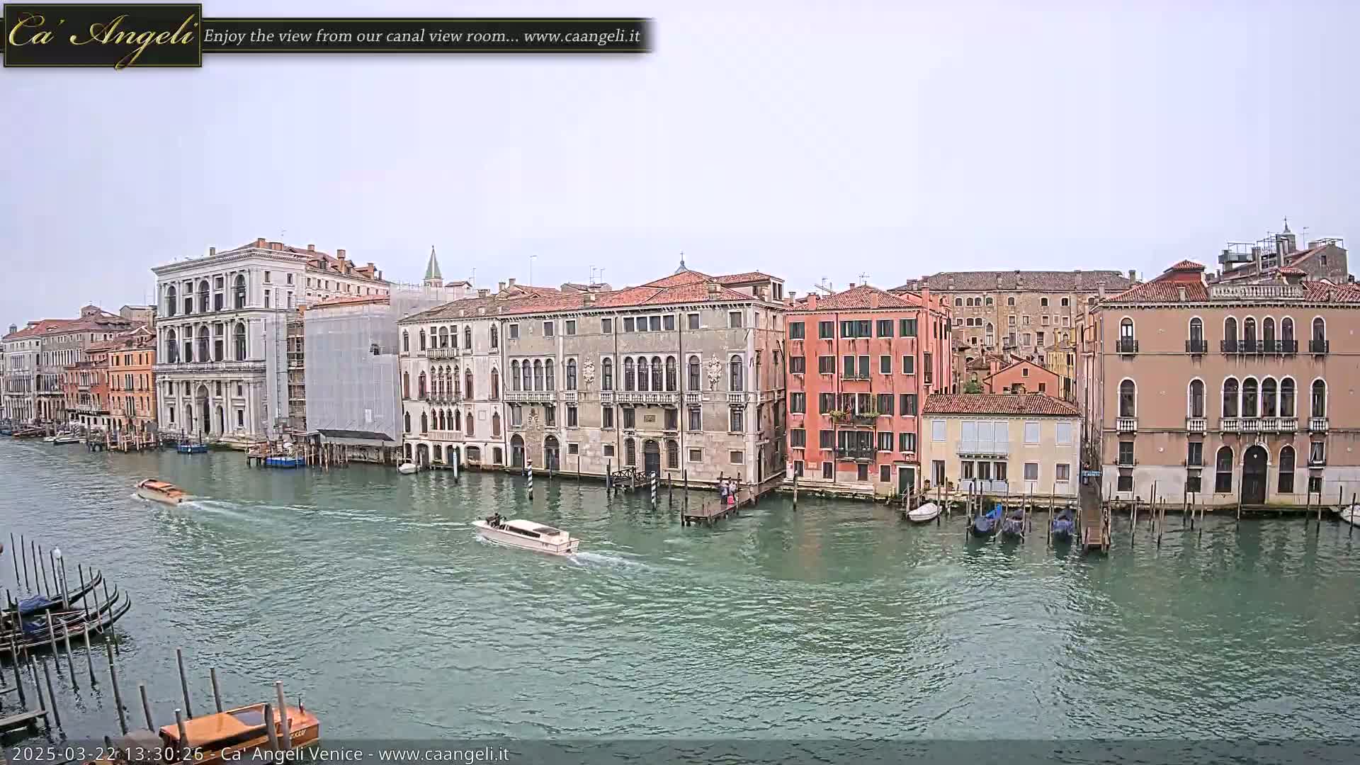 A canal in Venice, under an overcast sky, is lined with several multi-story buildings, and boats are traveling along the water.
