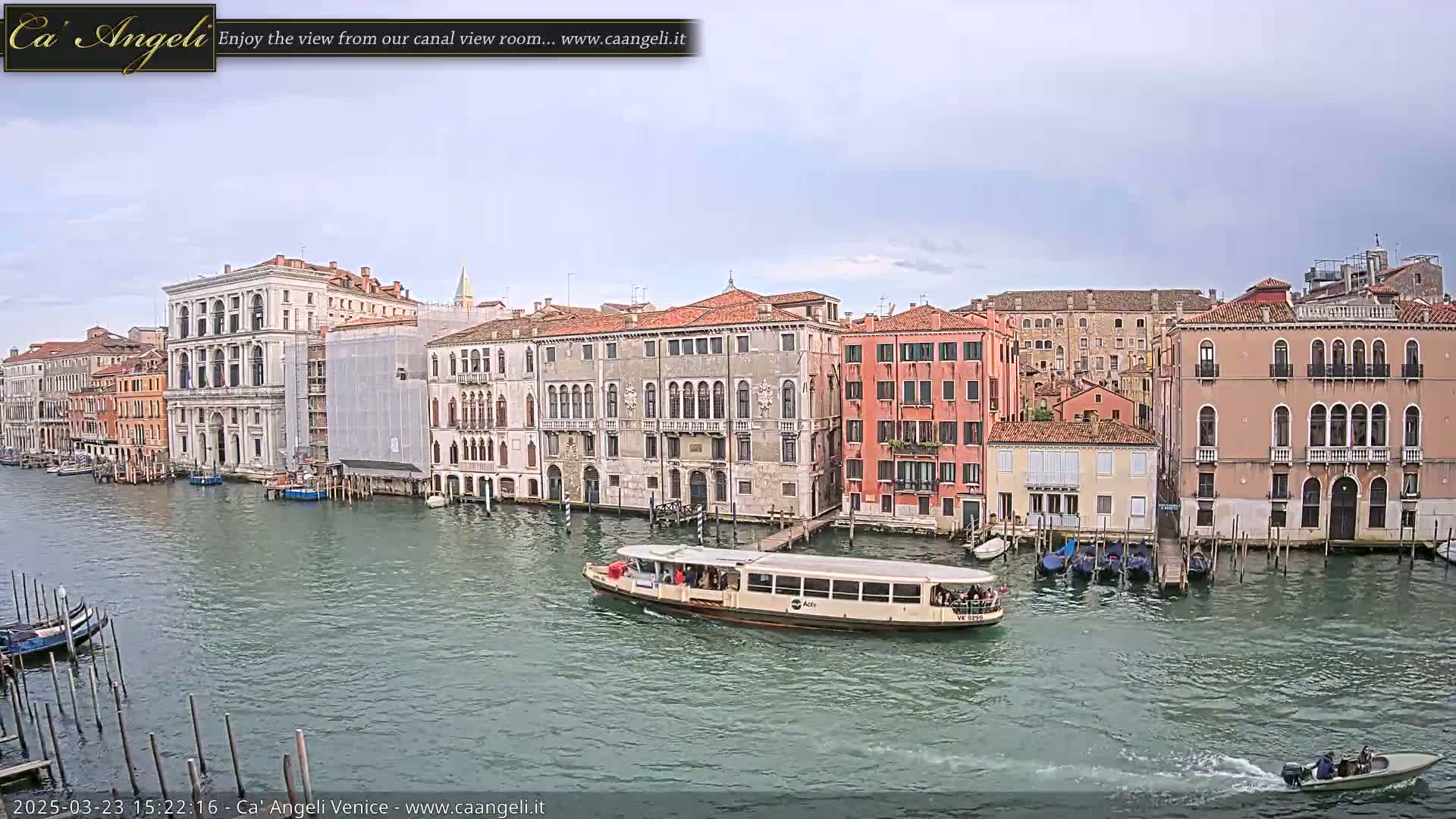 A water taxi travels down a canal in Venice, Italy, past several buildings under a partly cloudy sky.