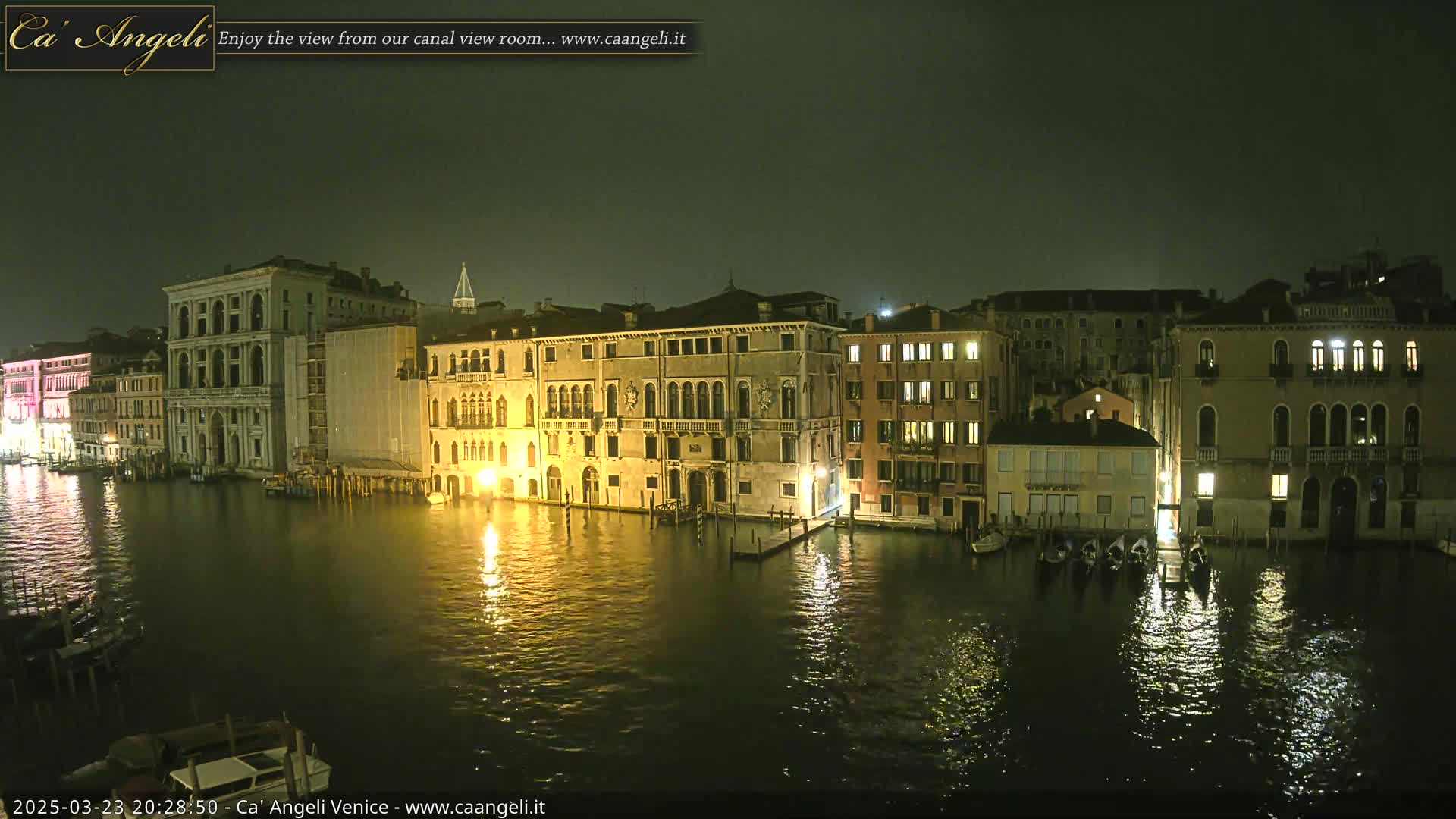A nighttime view of illuminated buildings lining a canal in Venice under a dark, overcast sky.