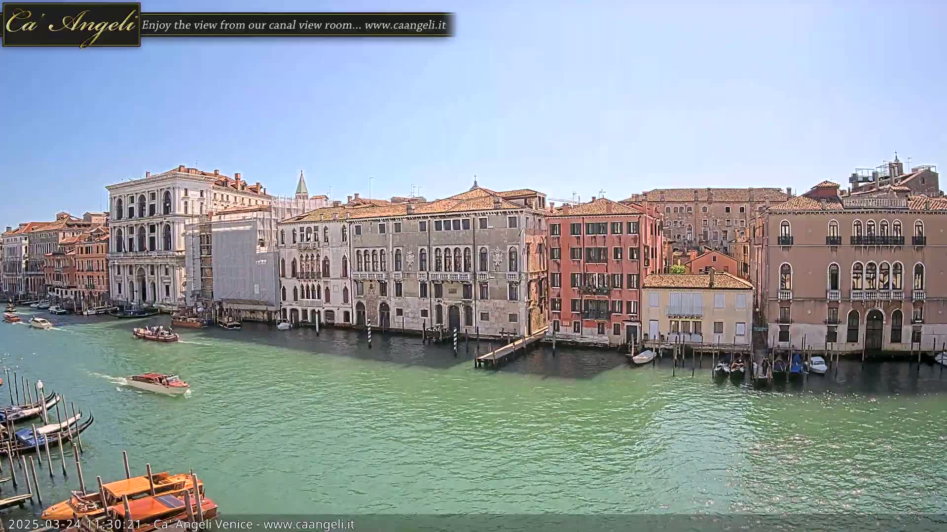 A sunny day in Venice shows a canal lined with historic buildings and several boats.