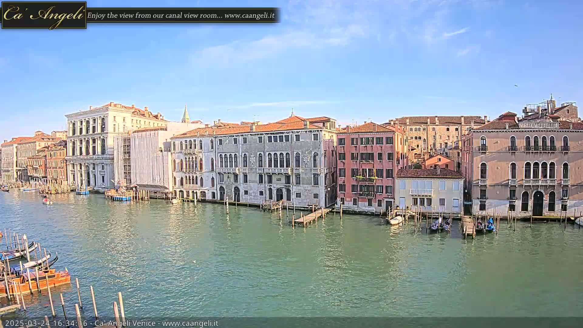 A sunny day in Venice shows several buildings lining a canal, with gondolas moored along the waterway.
