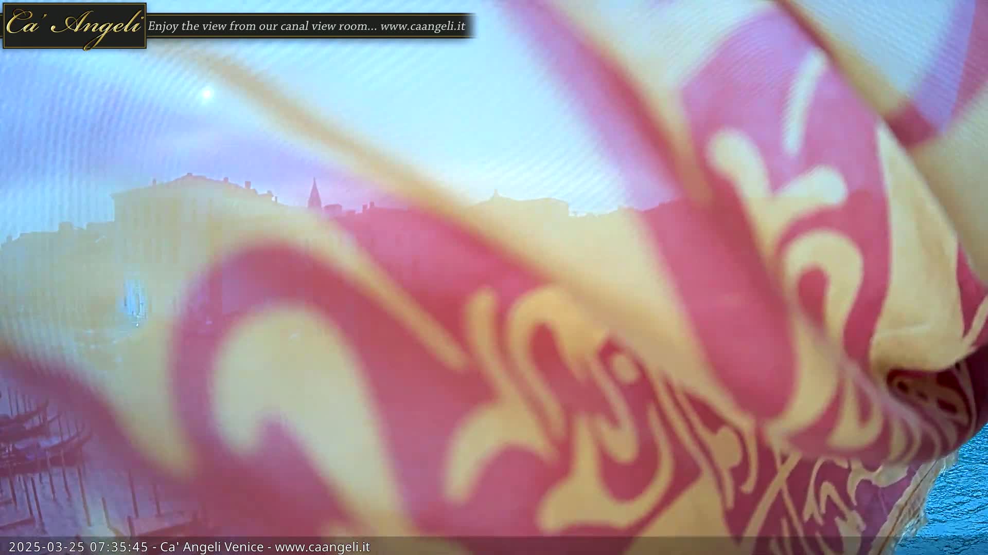 A blurry image of a city skyline is partially obscured by a pink and yellow patterned fabric in the foreground, under a bright, possibly sunny sky.