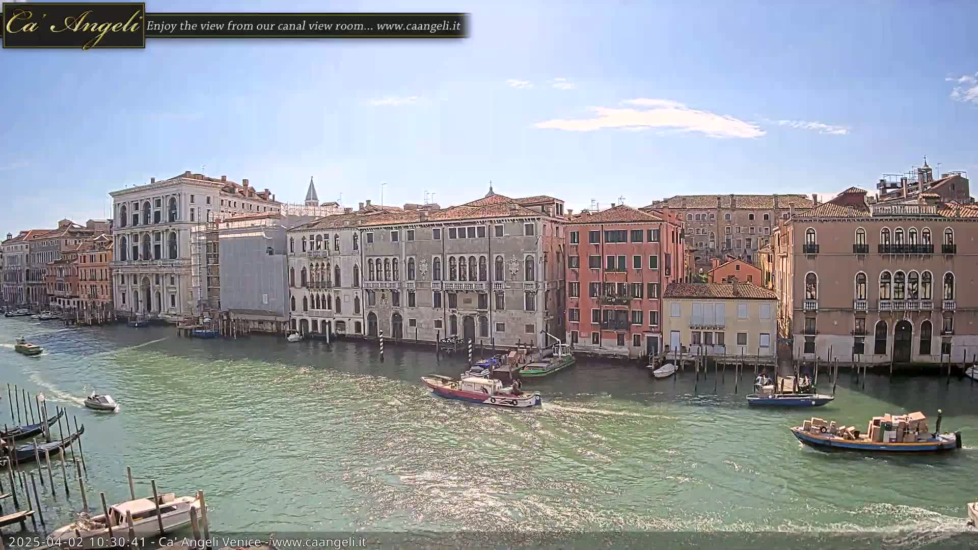 A sunny day in Venice shows a canal with numerous boats and buildings lining the waterway.