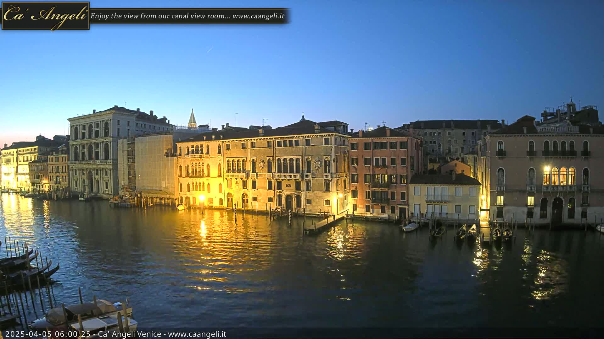 A twilight view of illuminated Venetian buildings lining a calm canal, with gondolas moored along the waterfront.