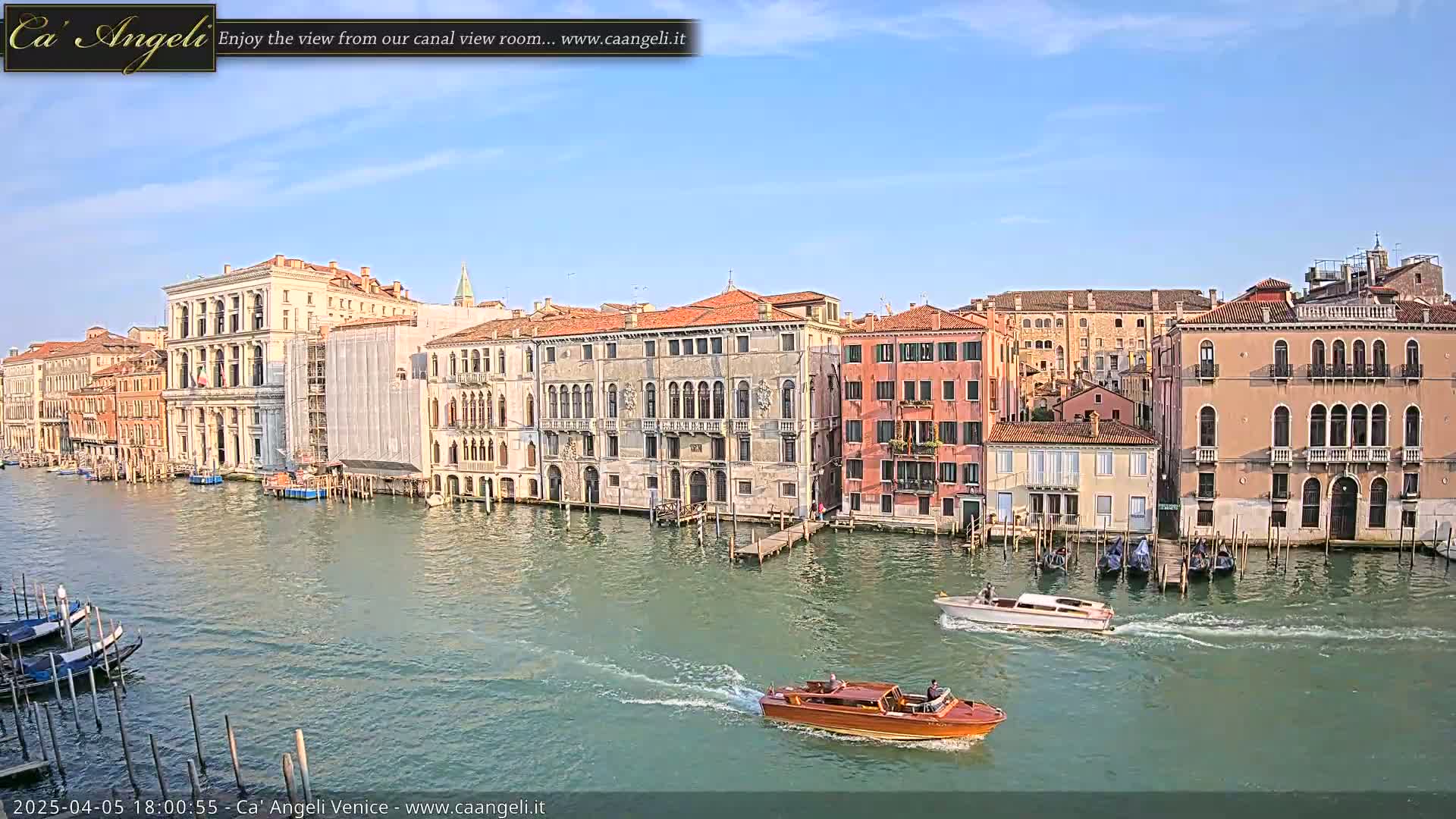 A sunny day reveals a Venetian canal lined with historic buildings, several gondolas, and motorboats traveling along the waterway.