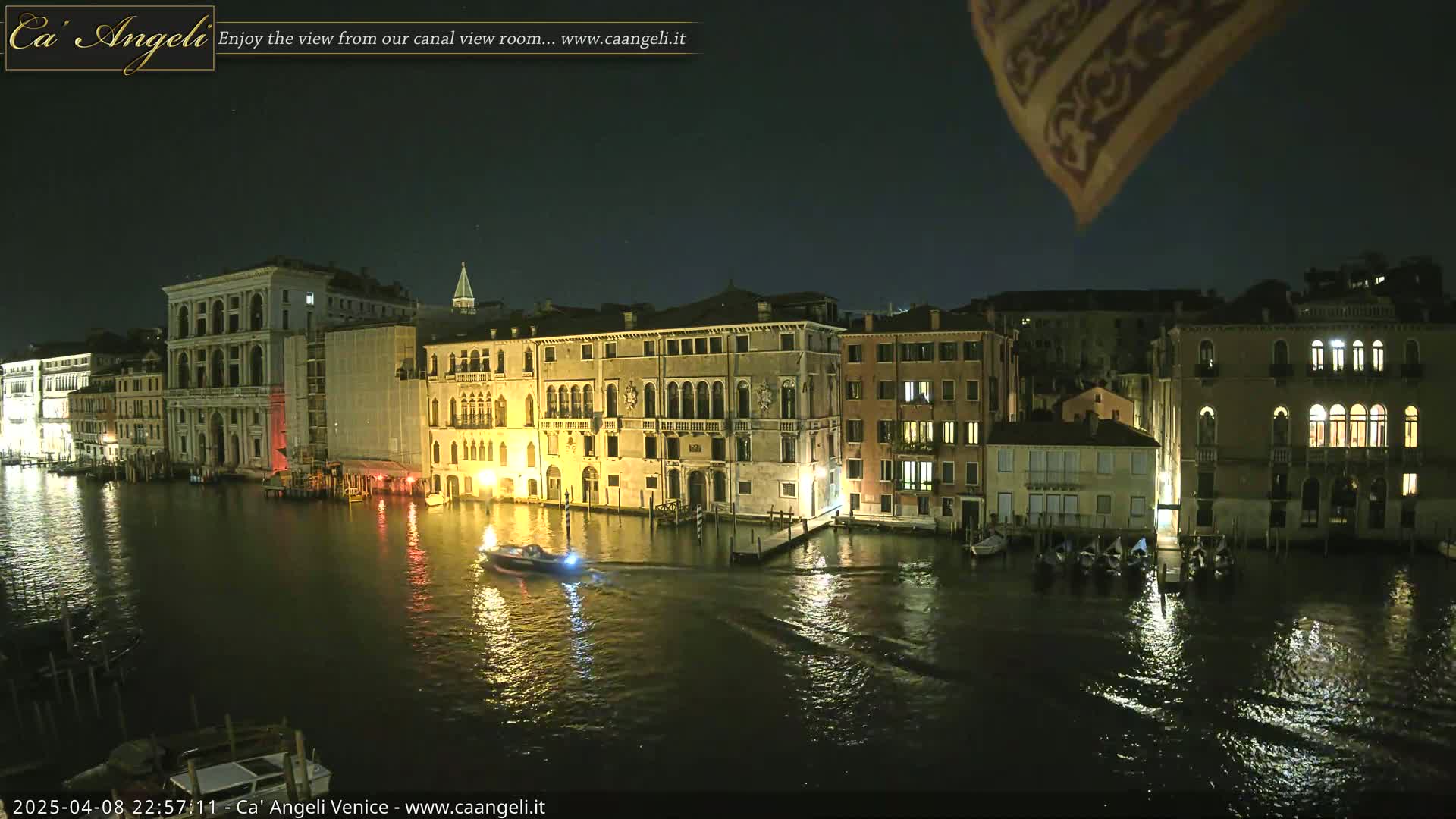 A nighttime view of a canal in Venice, with illuminated buildings lining the waterway and a small boat on the water.