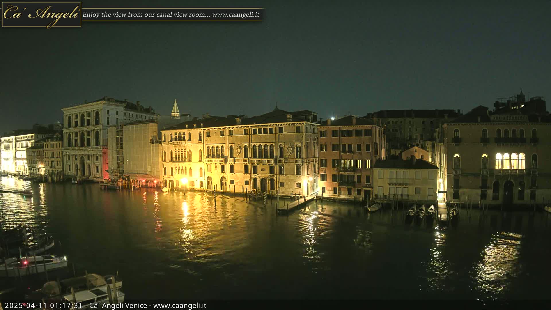 A nighttime view of illuminated buildings lining a canal in Venice, under a dark, clear sky.