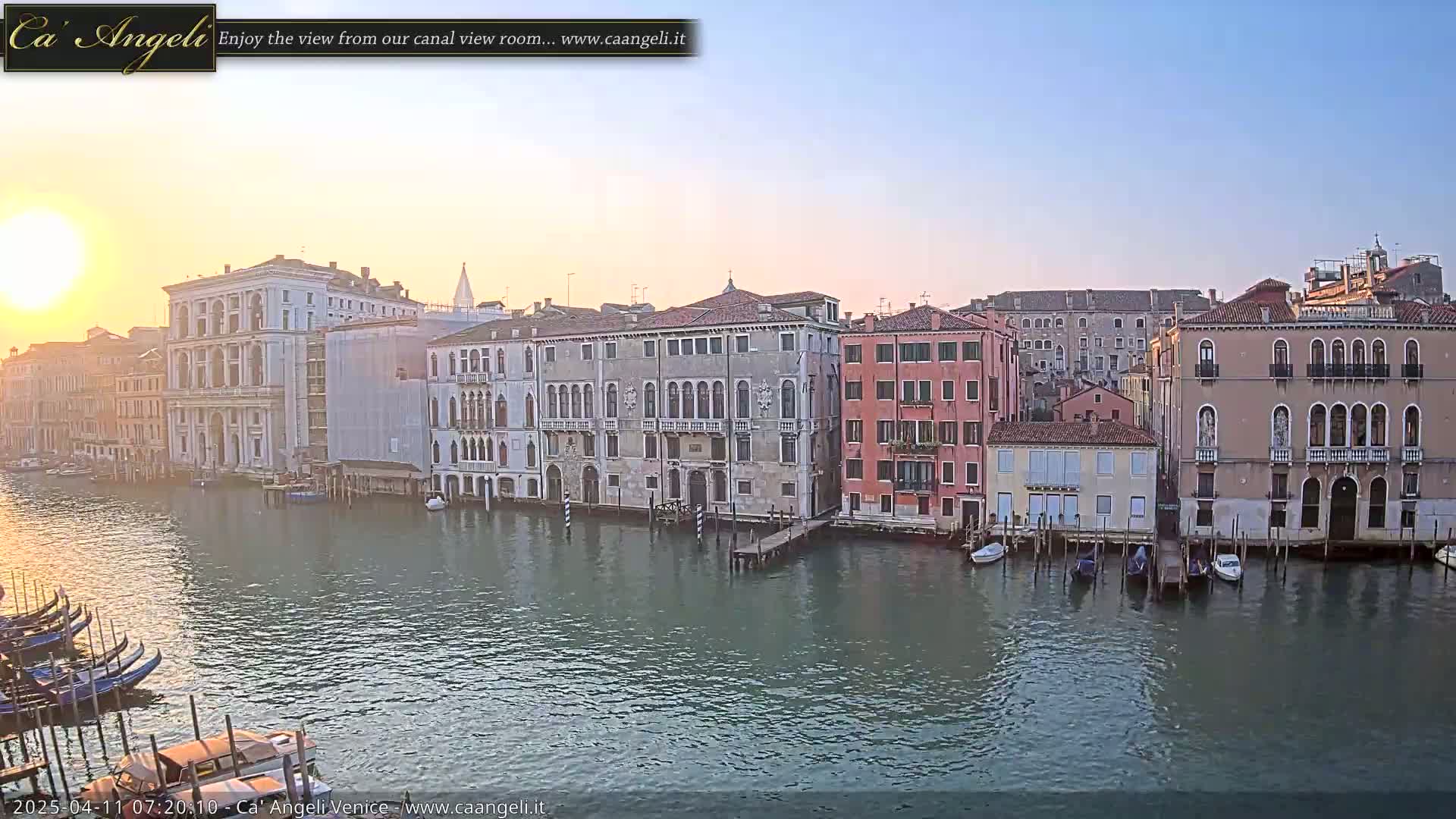 A tranquil sunrise illuminates a Venetian canal, lined with historic buildings and moored gondolas.