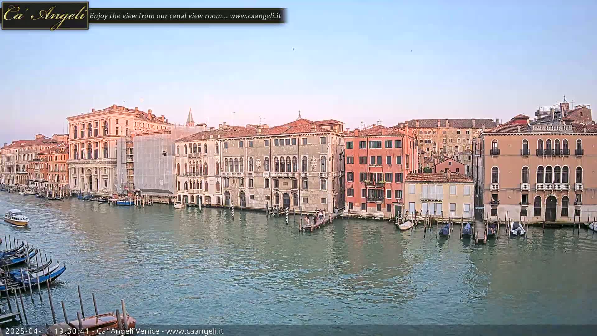 A calm canal in Venice, under a clear sky, is lined with several historic buildings and moored boats.