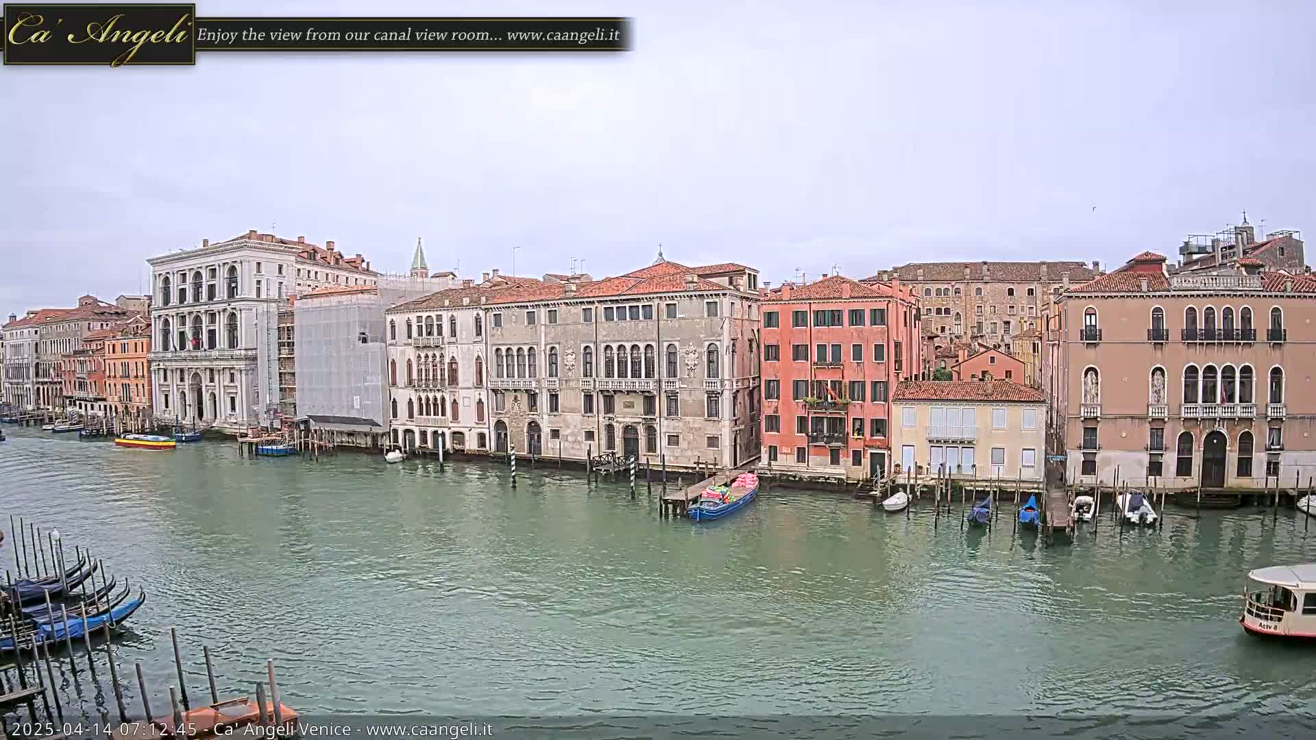 A canal in Venice, under an overcast sky, is lined with historic buildings, and several boats are moored along the waterfront.