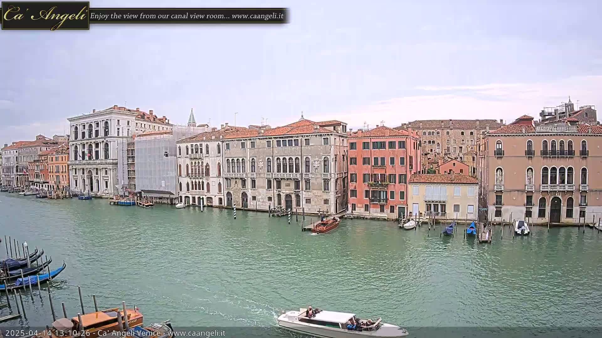 A canal in Venice, under an overcast sky, is lined with several historic buildings and boats.