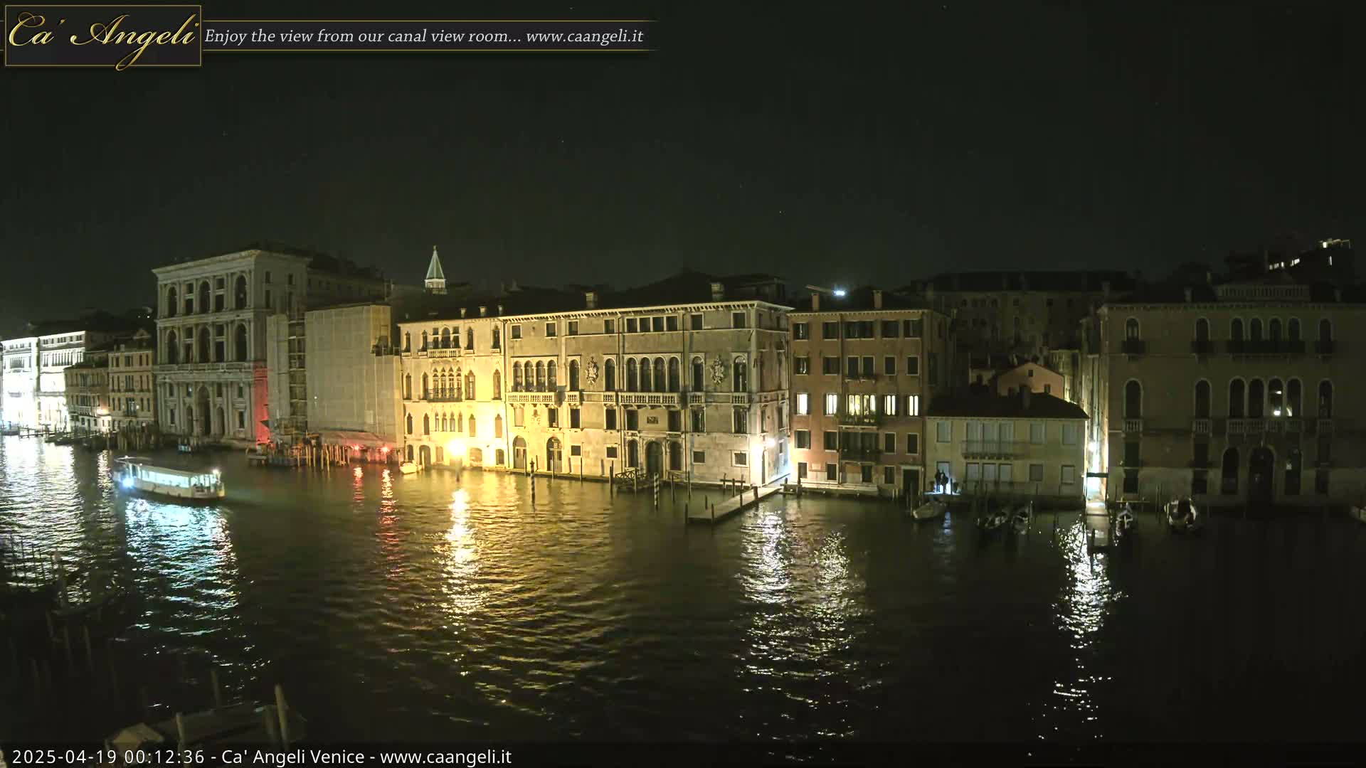 A nighttime view of a canal in Venice, showing illuminated buildings lining the waterway and a boat passing by.
