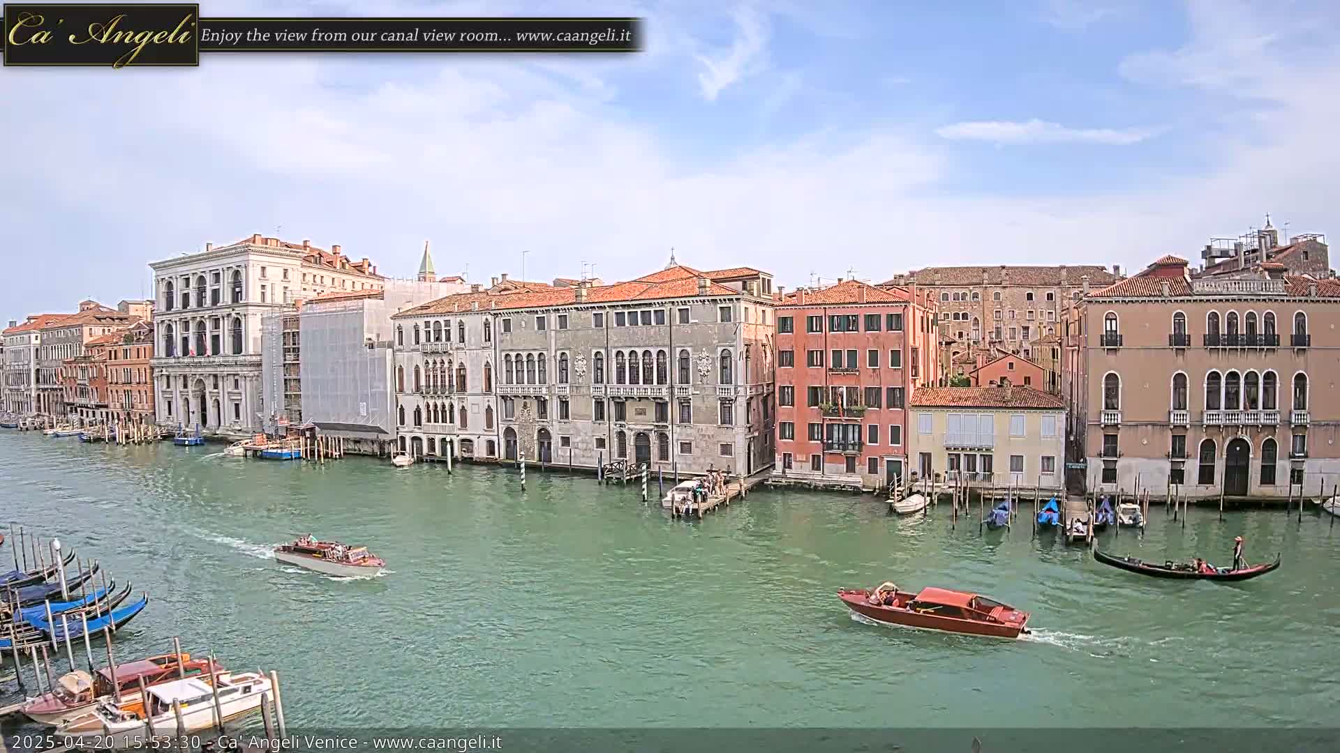 A sunny day in Venice shows several boats on a canal next to a row of buildings.