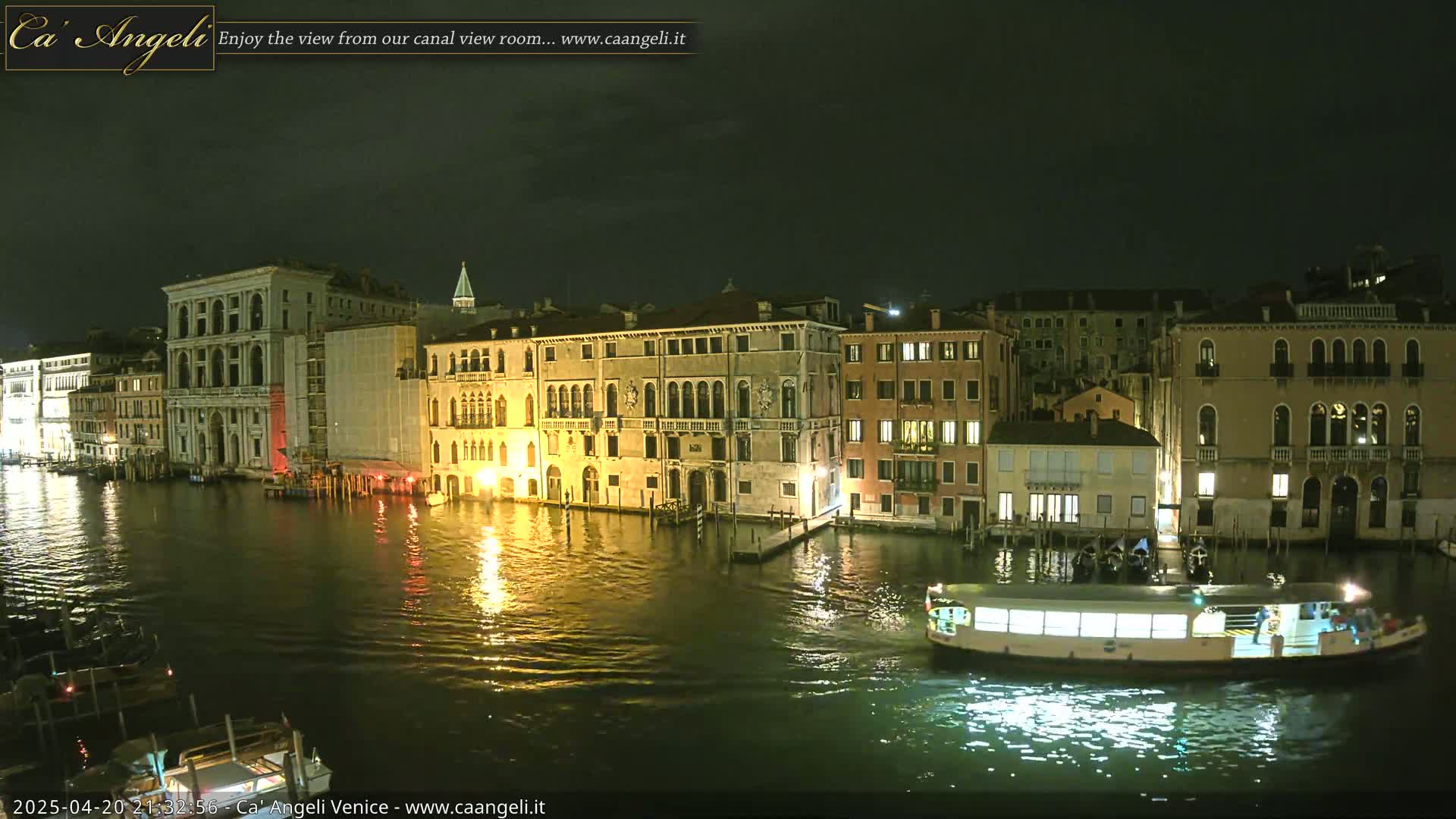 A nighttime view of a Venetian canal, showing illuminated buildings and a water taxi on the water.