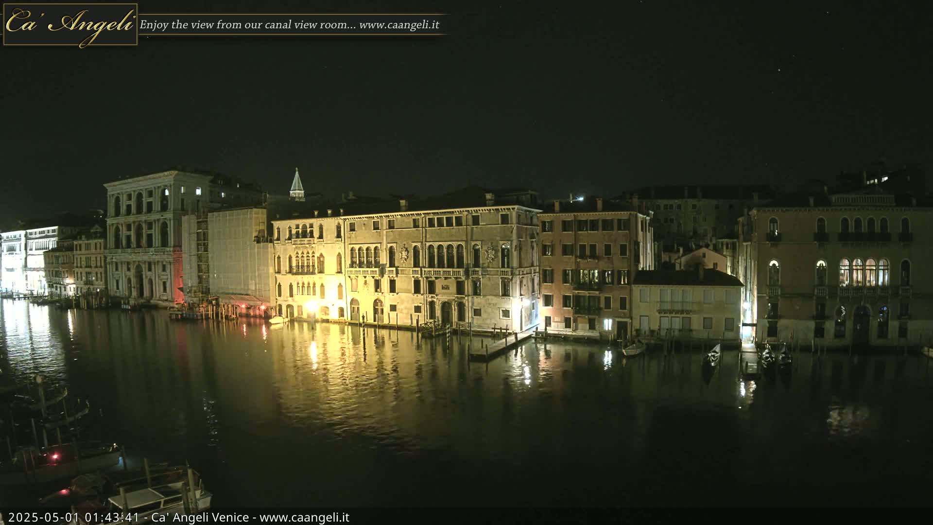 A nighttime view of a canal in Venice, Italy, with several buildings lit along its banks, and gondolas moored nearby under a clear, starry sky.