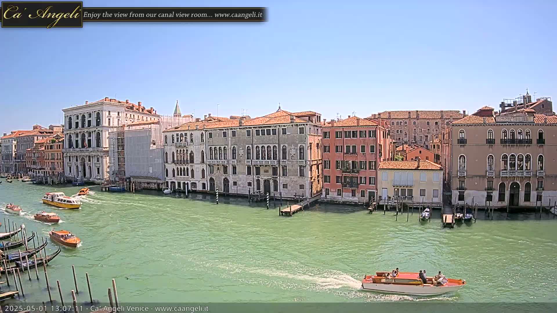 On a sunny day, several boats are traveling on a canal in Venice, Italy, lined with historic buildings.