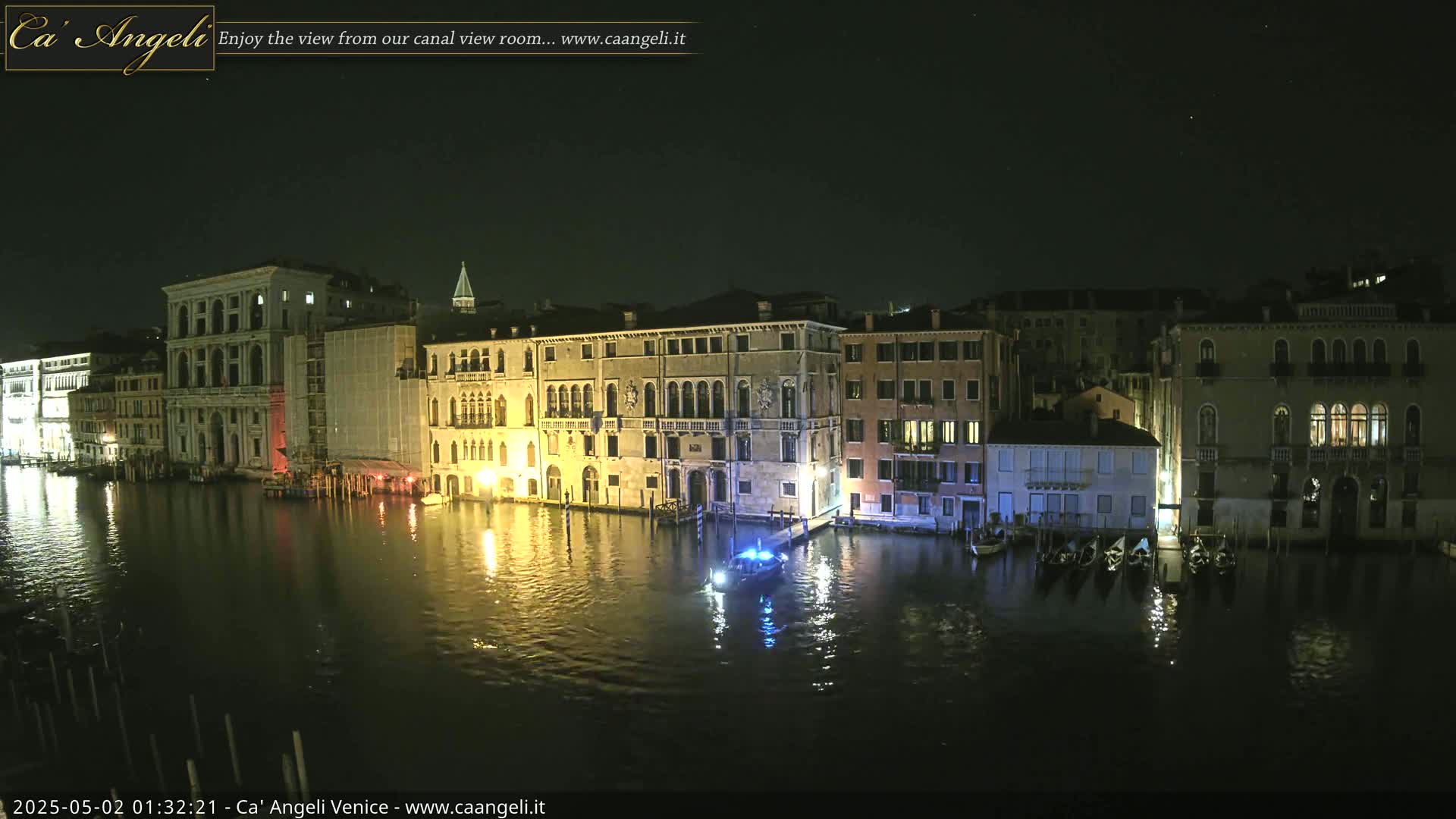 Illuminated buildings line a dark canal at night, with a small boat on the water.