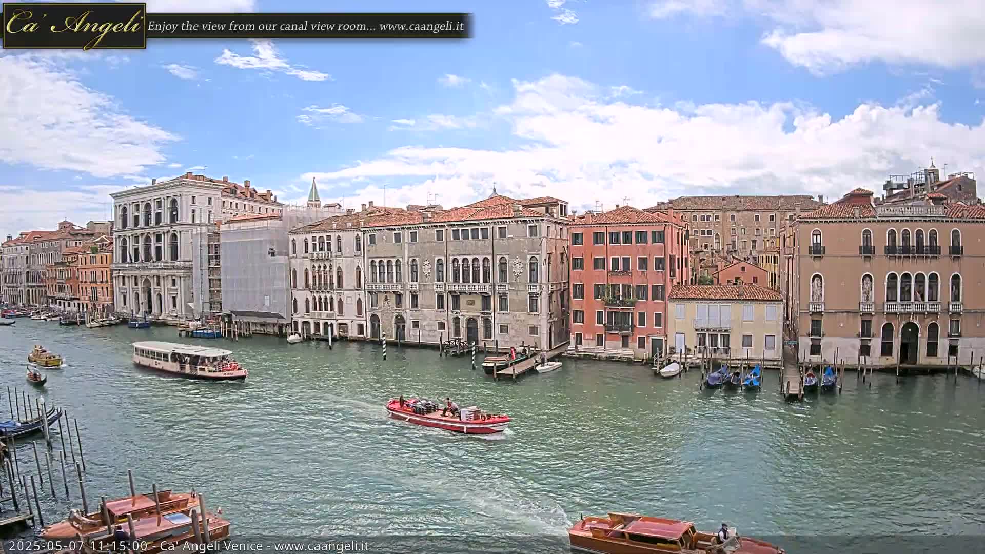 A sunny day in Venice shows several boats on a canal lined with tall, historic buildings.