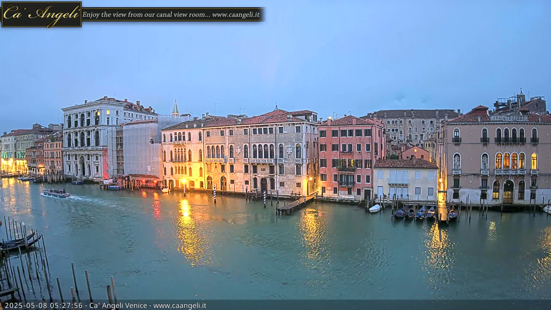 A tranquil canal in Venice at twilight, lined with historic buildings reflecting in the calm water, with a few gondolas moored along the banks.
