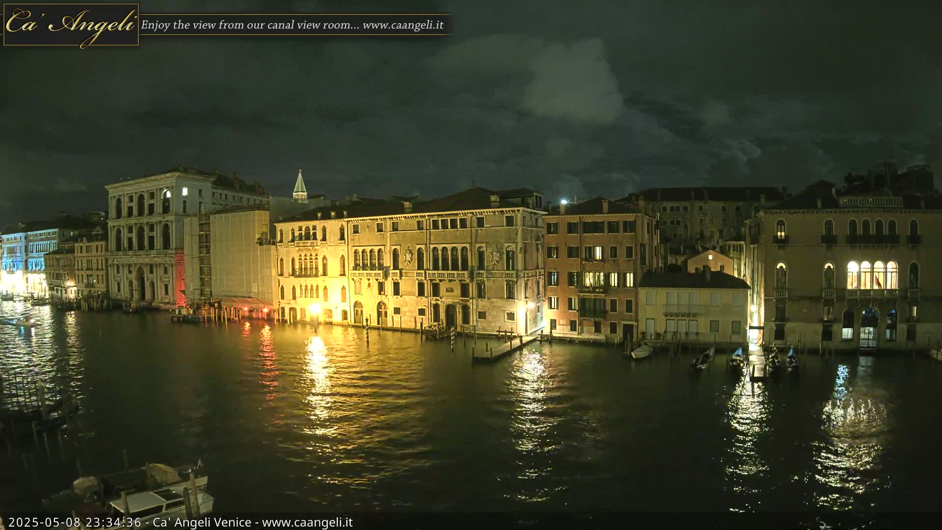 A nighttime view of illuminated buildings along a calm canal in Venice under a partly cloudy sky.