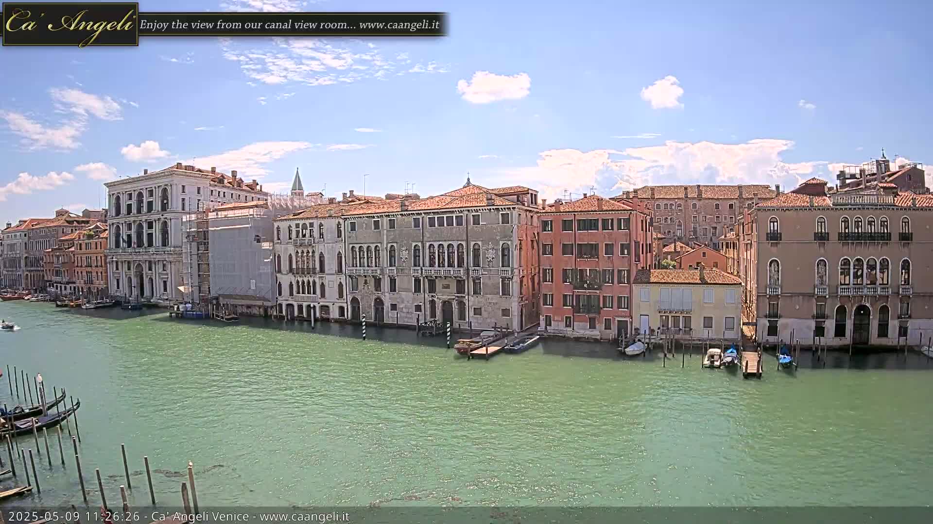 A sunny day in Venice shows several buildings lining a canal, with gondolas moored along the edges.