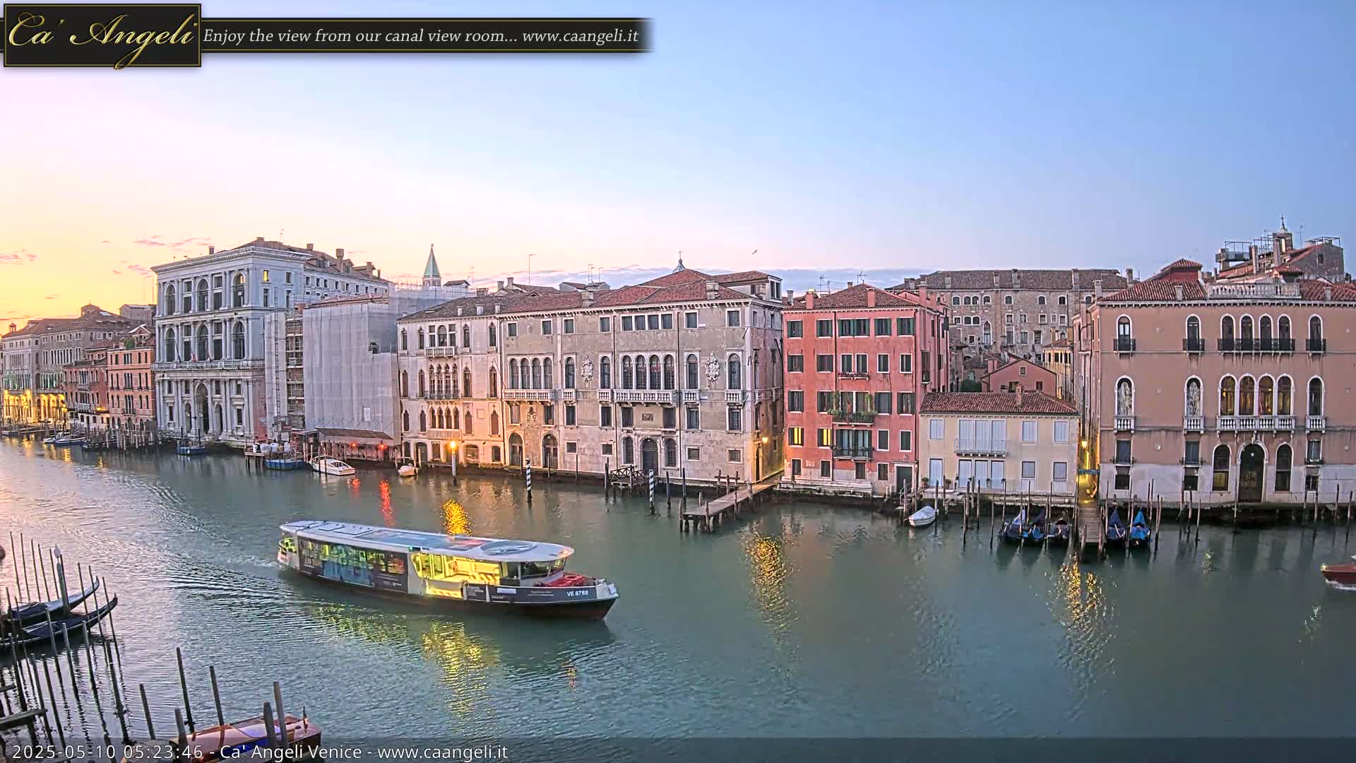 A calm canal in Venice at dawn, lined with historic buildings, with a water bus traveling down the waterway.