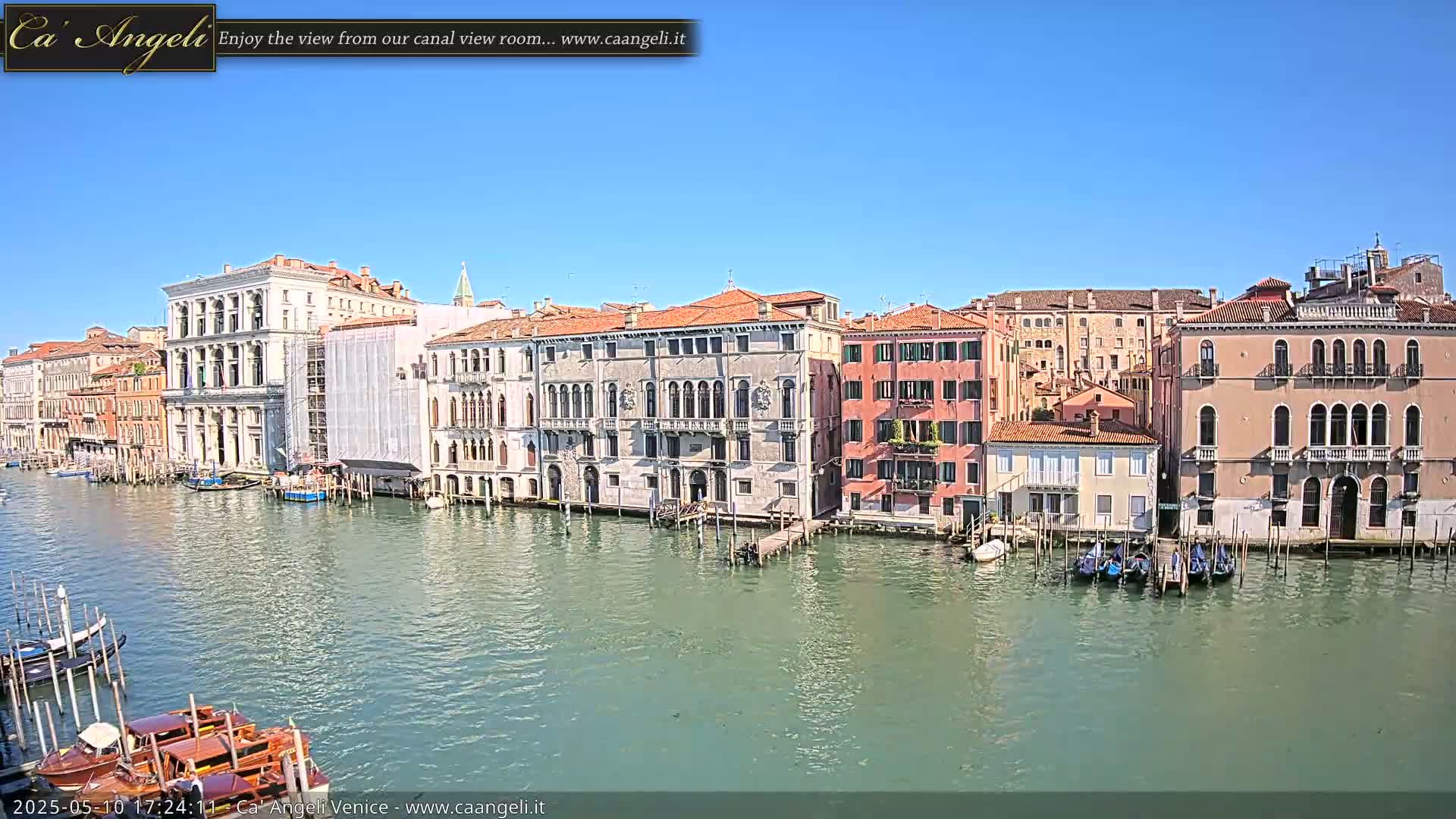 A sunny day in Venice shows several colorful buildings lining a canal, with gondolas moored along the waterfront.