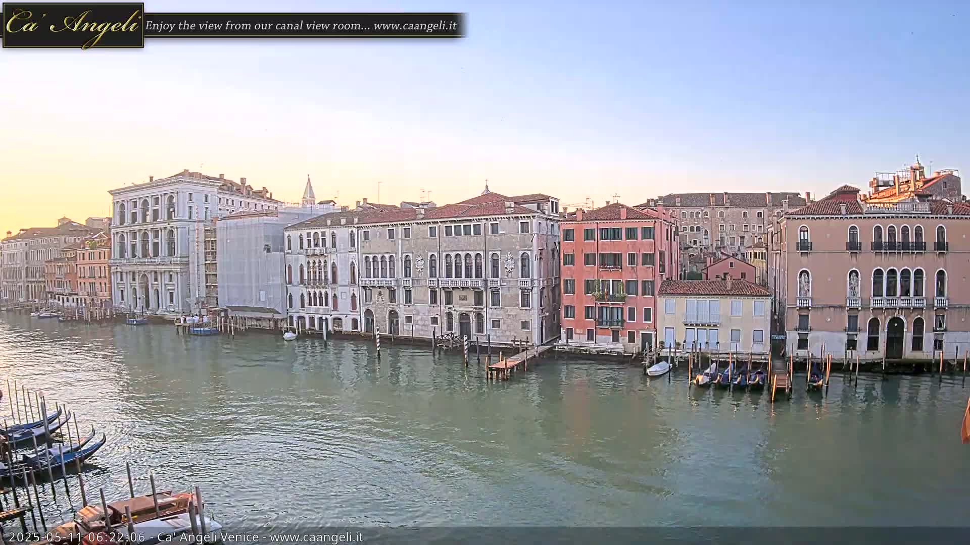 A calm canal in Venice, Italy, is lined with historic buildings under a clear, light-blue sky.
