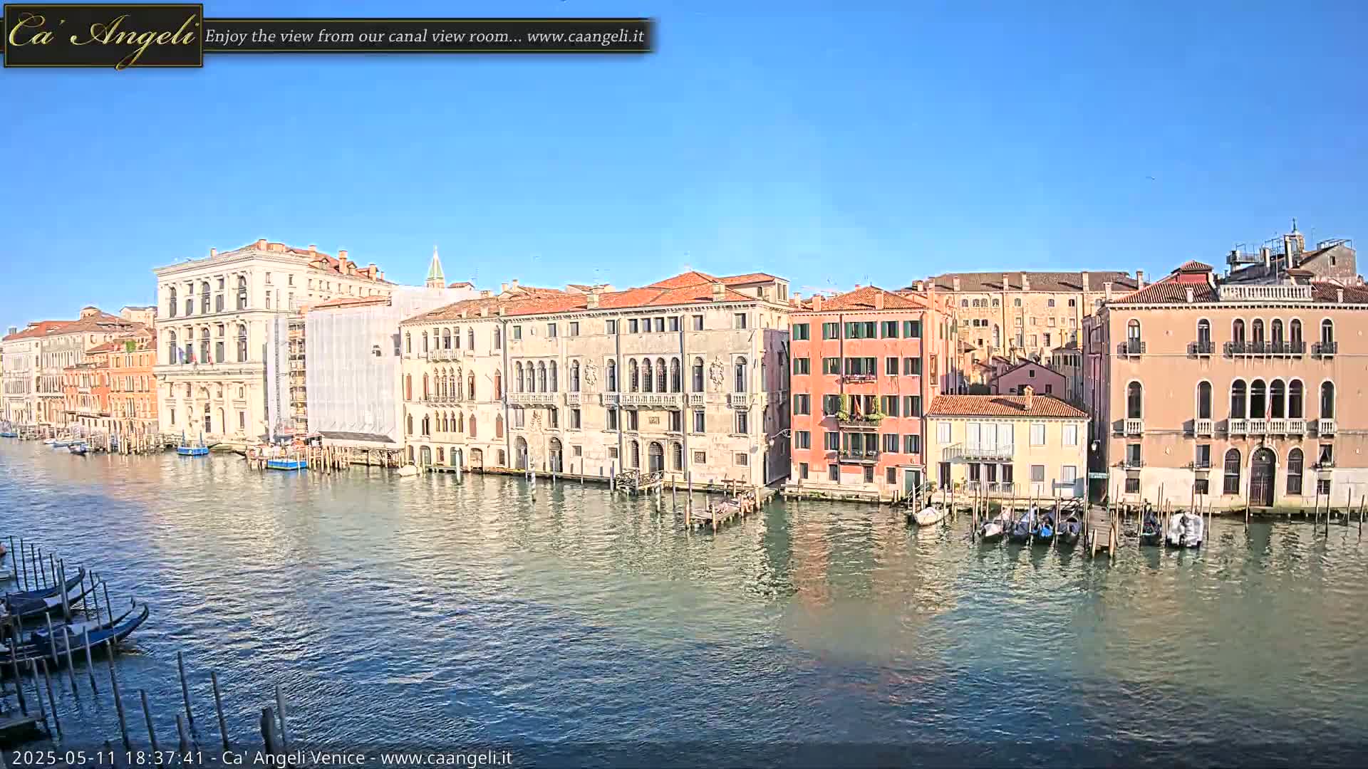 A sunny day reveals a Venetian canal lined with historic buildings, several gondolas are moored along the waterfront.