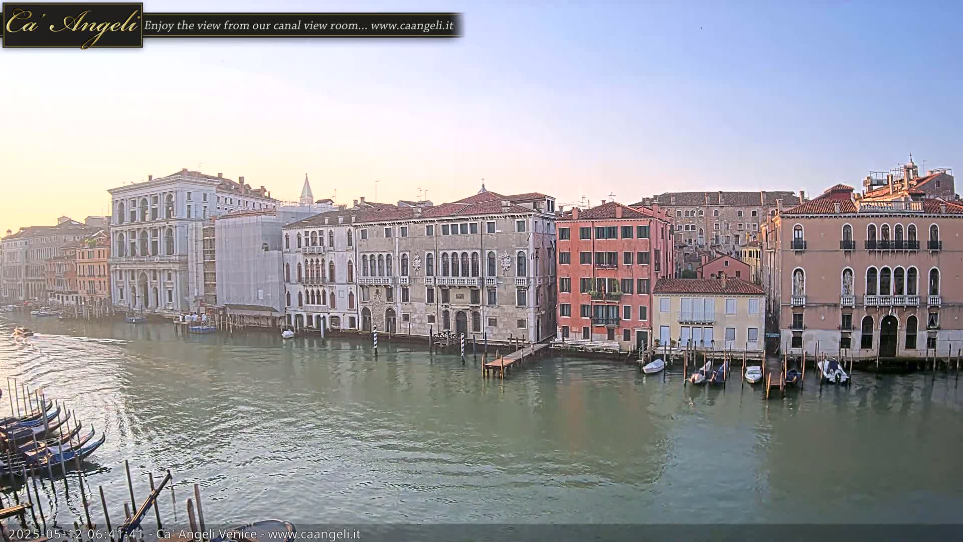 A calm canal in Venice, Italy, is lined with several historic buildings under a clear, light-blue sky.
