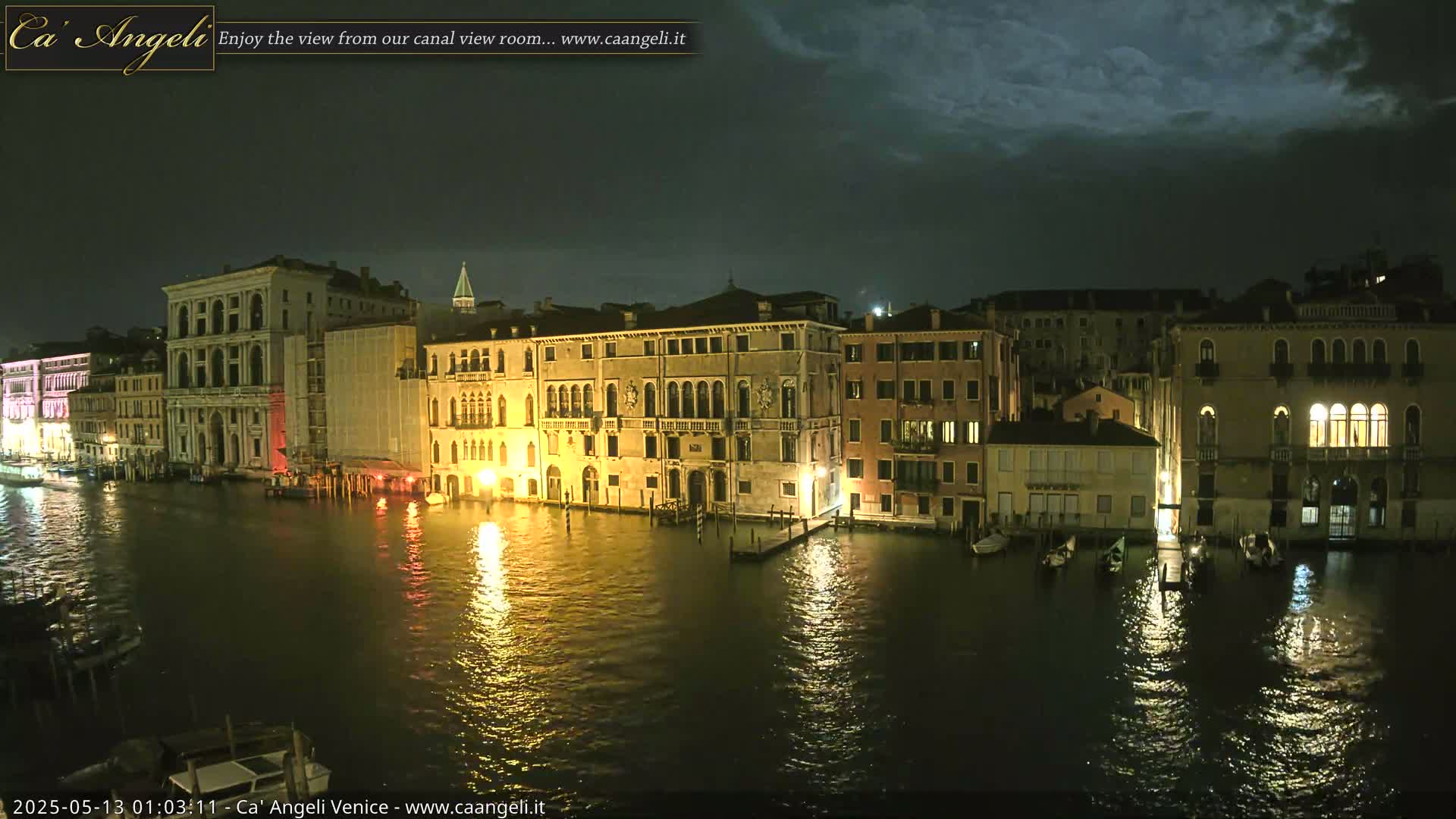 Illuminated buildings line a canal at night under a partly cloudy sky.