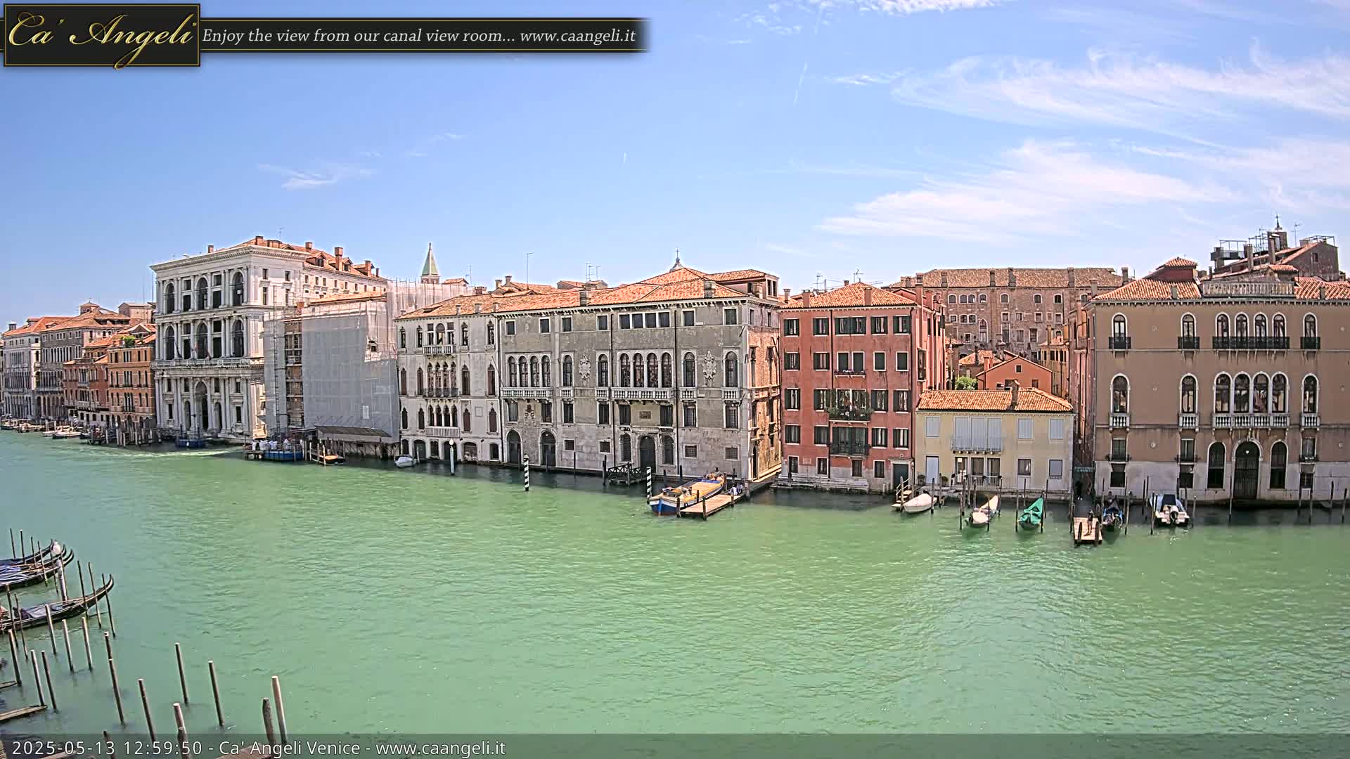 A sunny day in Venice shows several colorful buildings lining a canal, with gondolas moored along the water's edge.