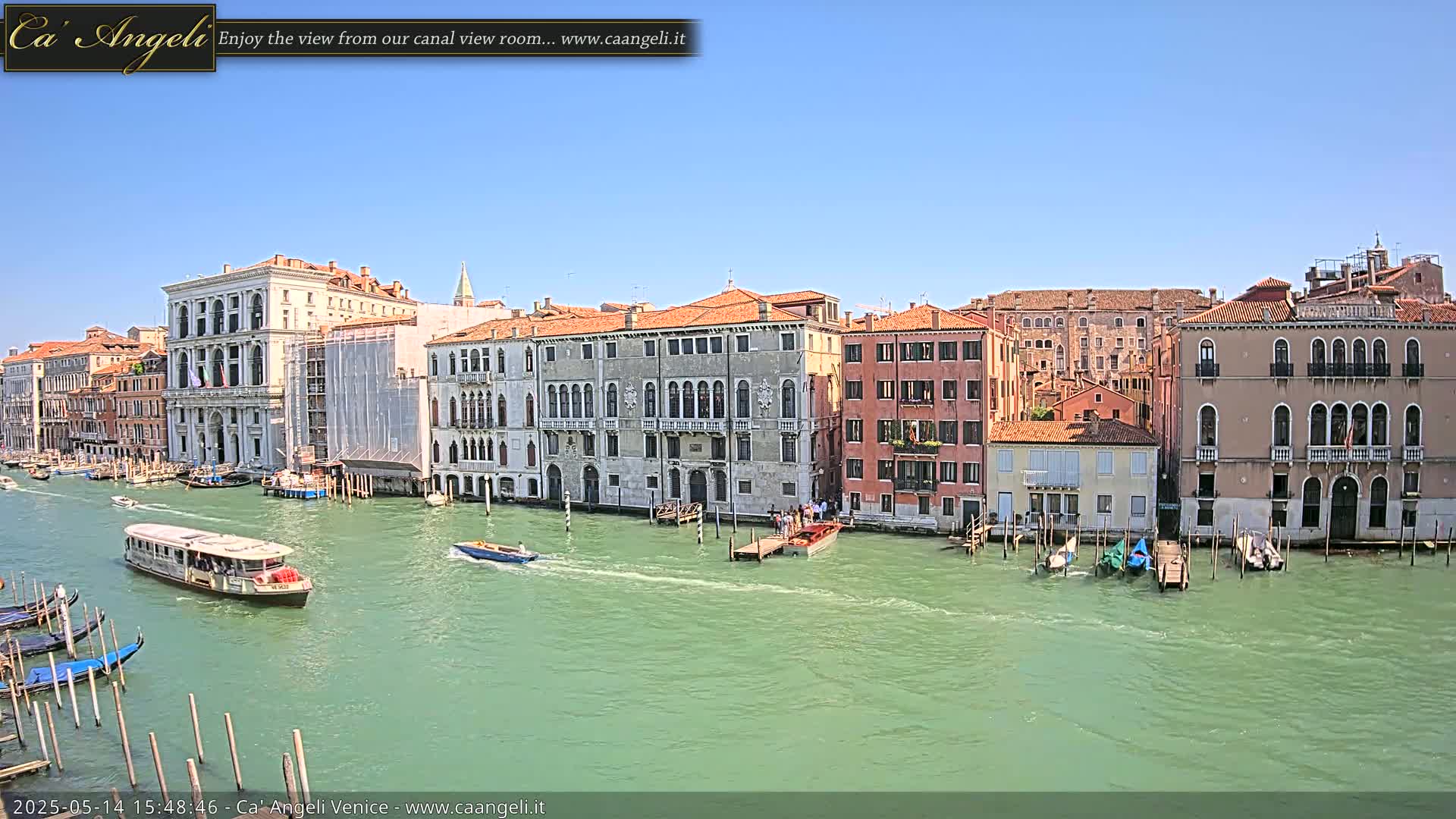 A waterway filled with boats is lined with several multi-story buildings under a clear blue sky.