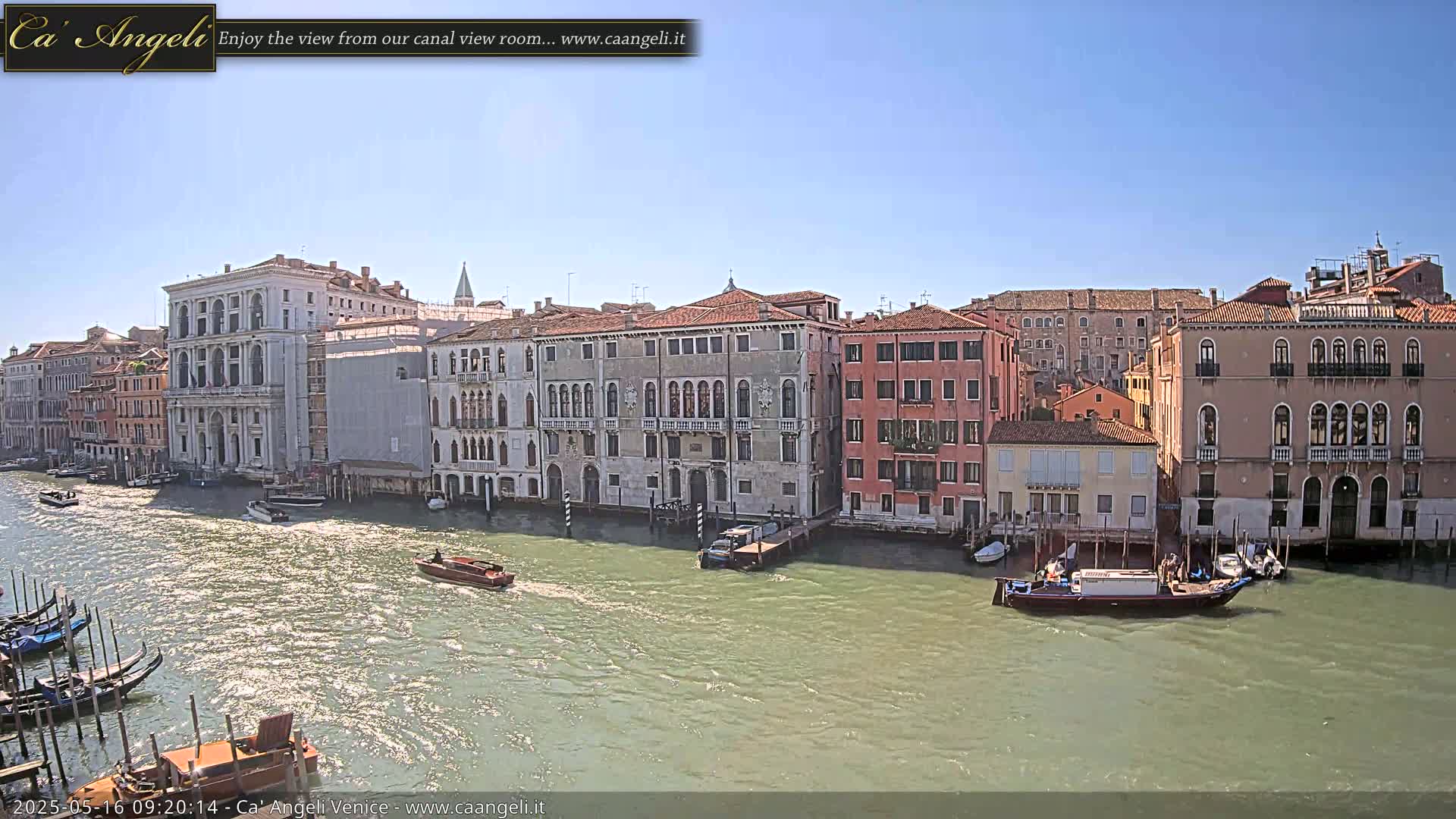 A sunny day in Venice shows a canal with gondolas and boats, lined with several multi-story buildings.